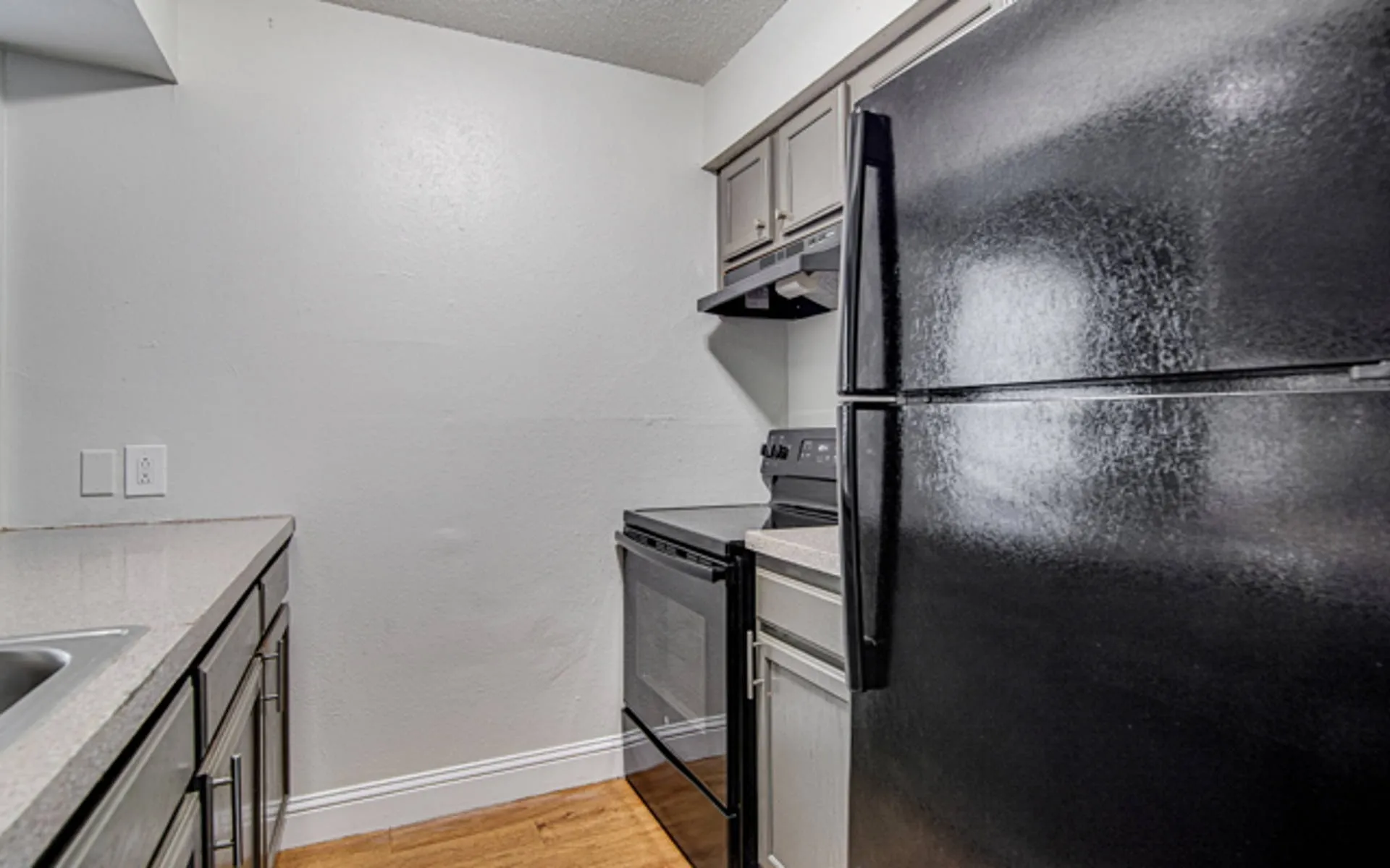 Kitchen featuring wood-finish flooring, gray cabinetry, a stainless steel sink, and black appliances including a refrigerator and range