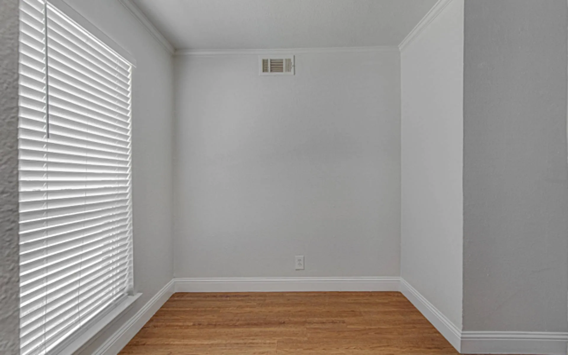 Wood-finish flooring, white walls, and a window with blinds