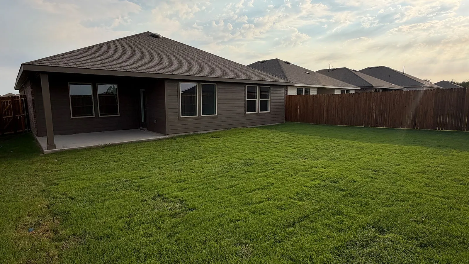 Expansive backyard with a covered patio, privacy fencing, and a manicured lawn