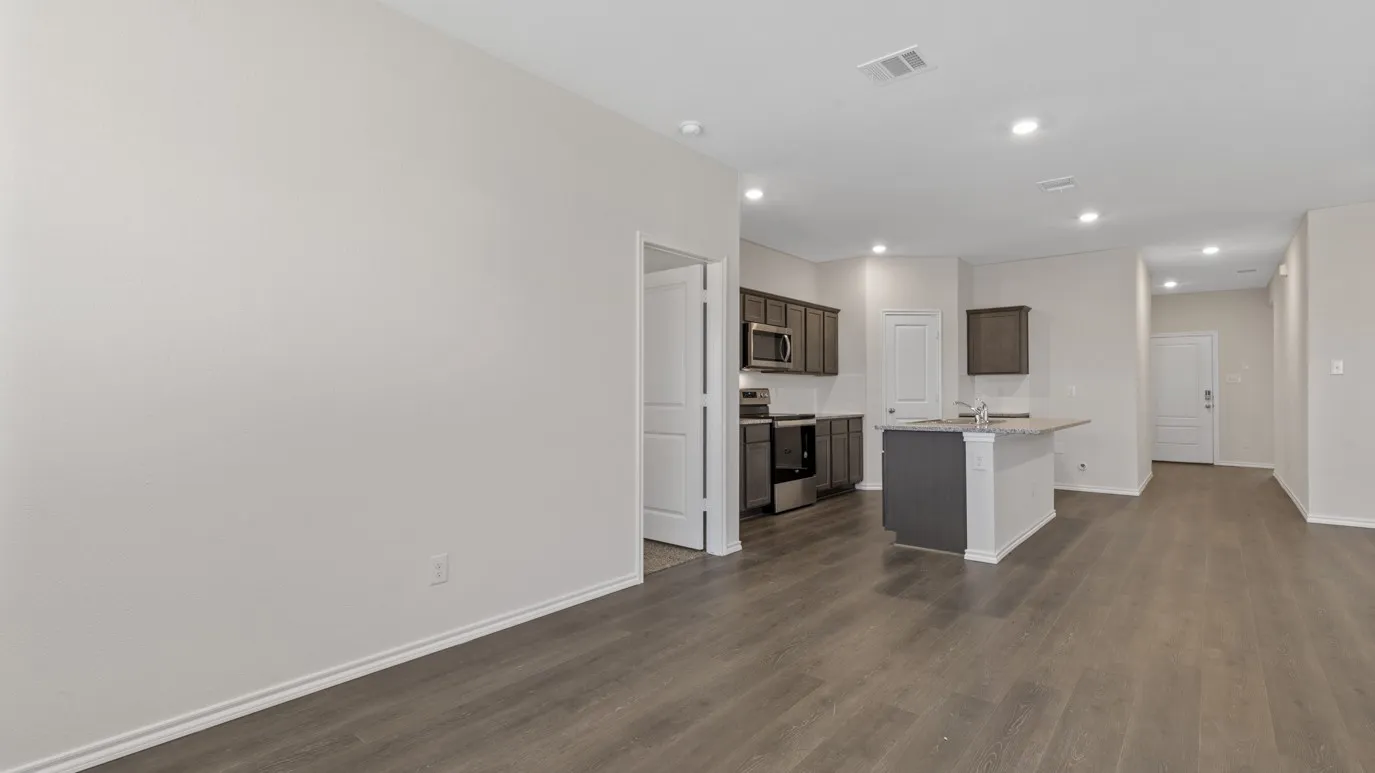Open-concept living area with dark wood-finish flooring, recessed lighting, and a kitchen featuring dark cabinetry, stainless steel appliances, and a breakfast bar island