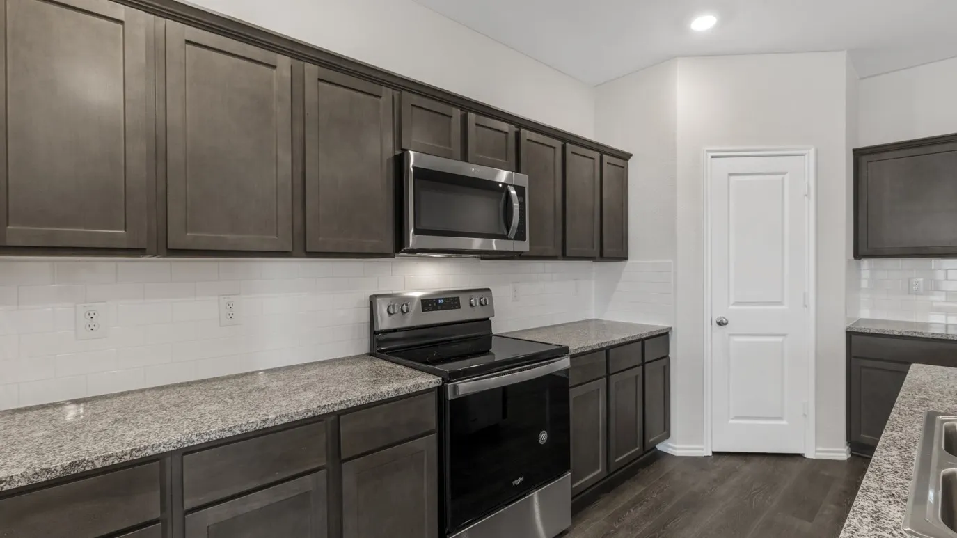 Dark wood-finish cabinetry, light speckled countertops, stainless steel appliances, and white subway tile backsplash