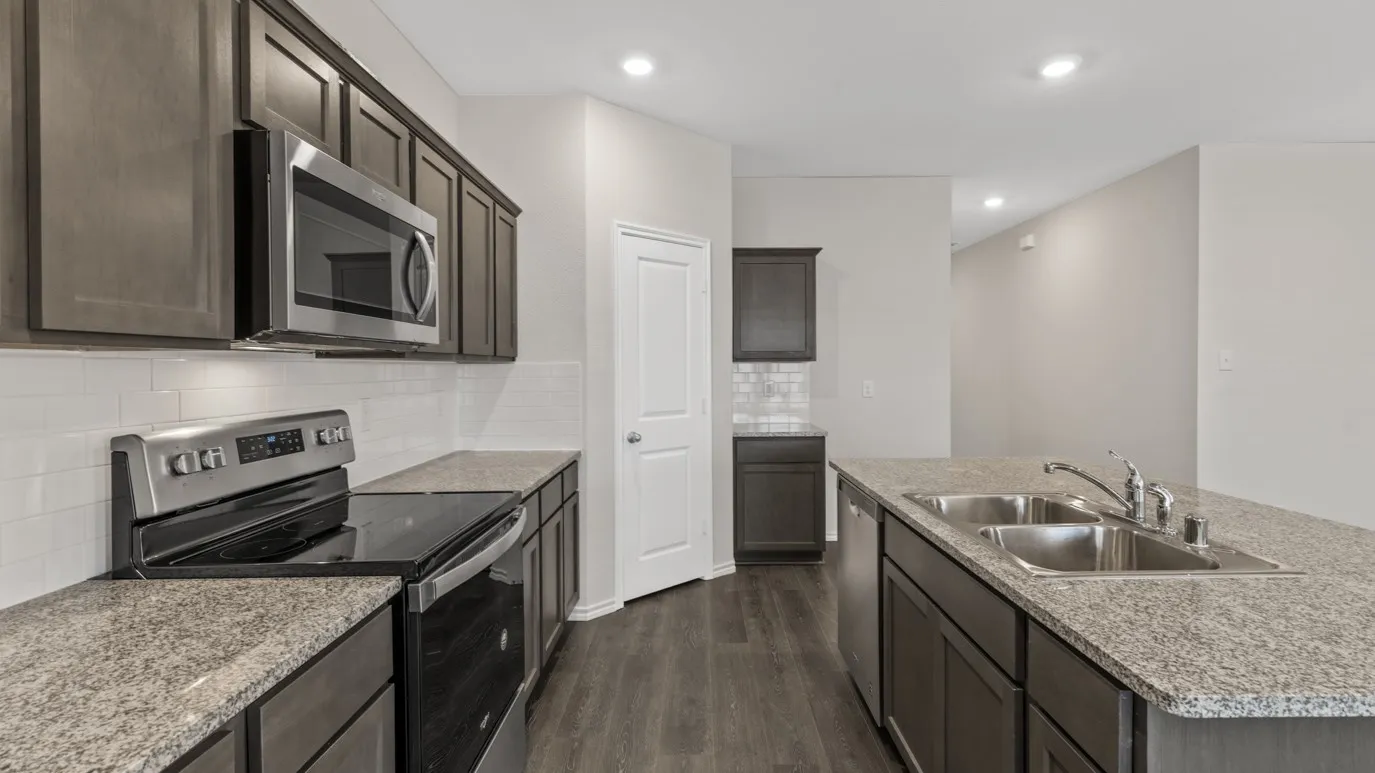 Kitchen featuring dark wood-finish cabinetry, light speckled countertops, stainless steel appliances, and wood-finish flooring