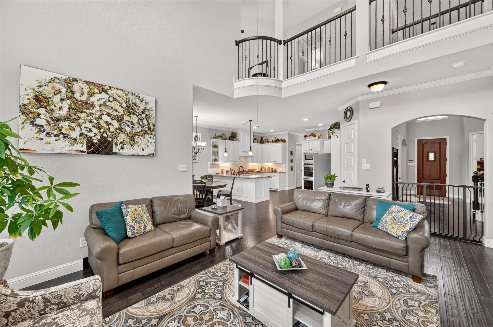 Open-concept living area featuring soaring two-story ceilings, abundant natural light from multiple windows, and a central kitchen with stainless steel appliances and white cabinetry