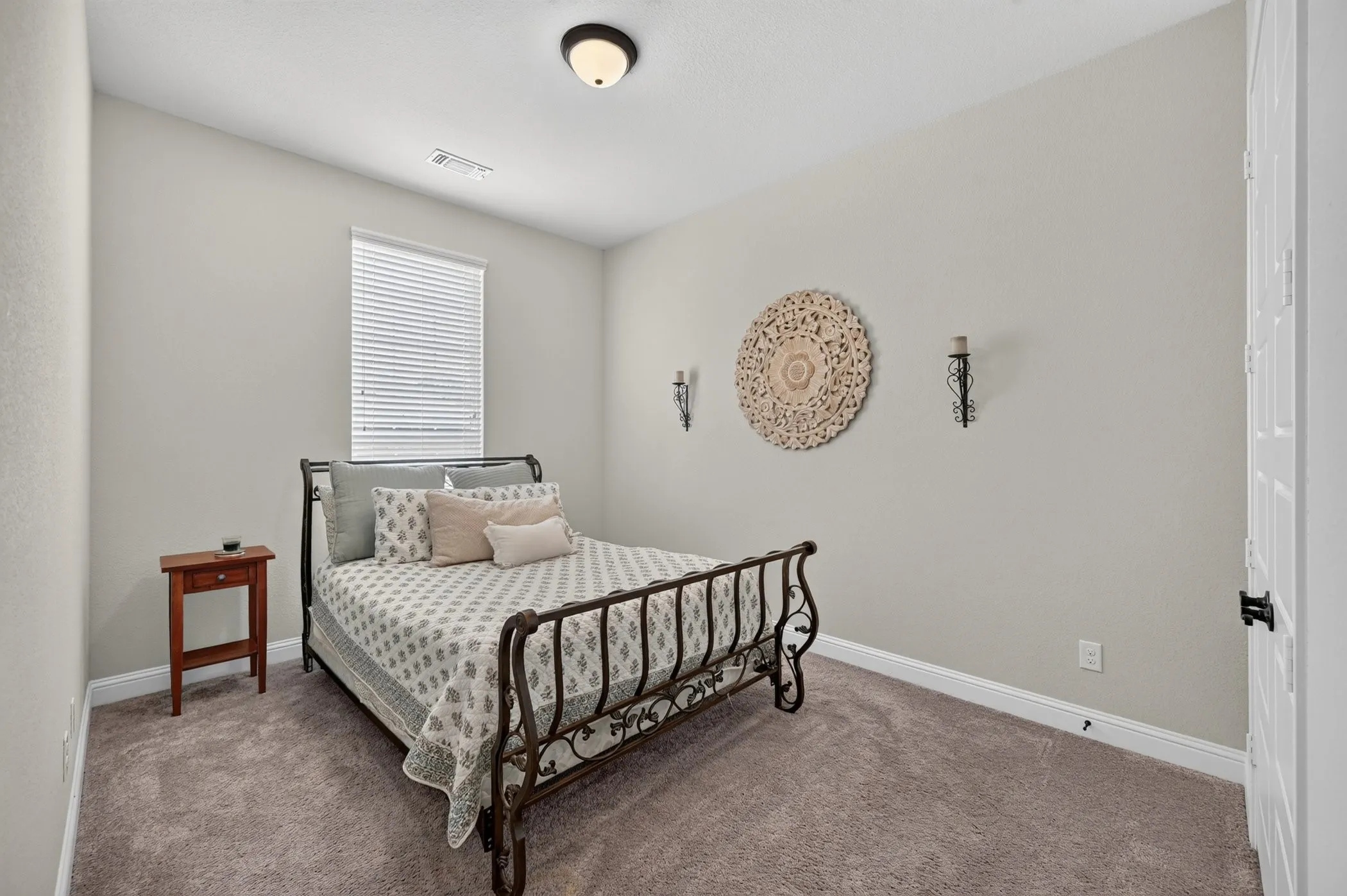 Bright secondary bedroom featuring a cast-iron bed frame, carpet flooring, and natural light from a horizontal-blinds window