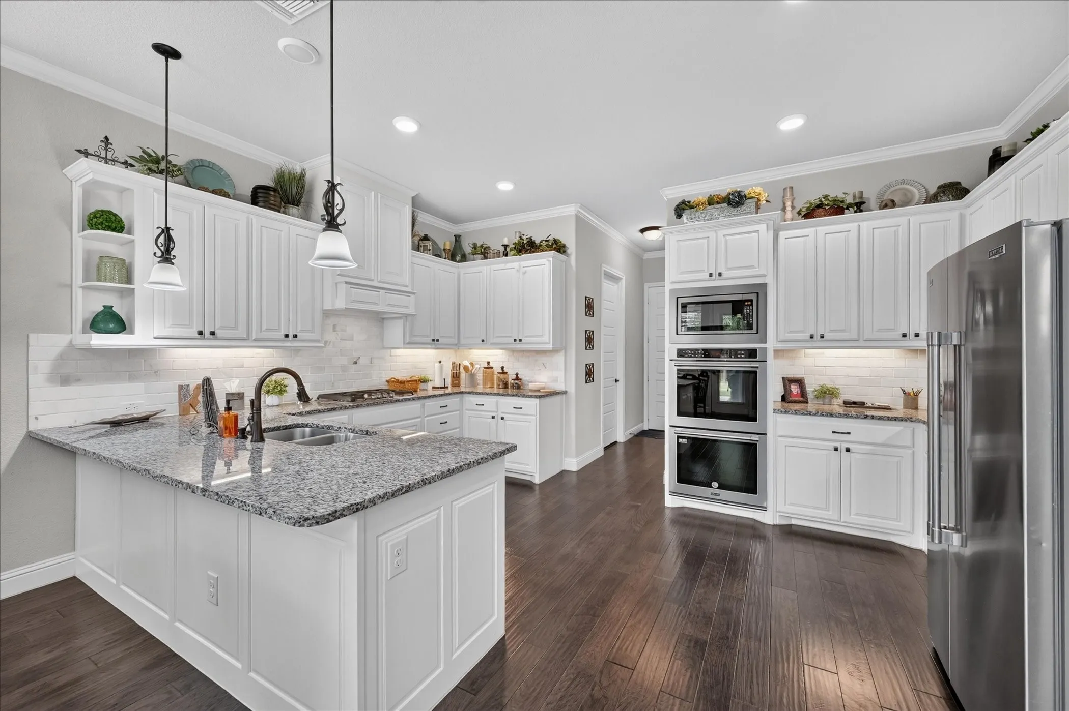 Kitchen featuring a central island with a dual-basin sink, white cabinetry with crown molding, stainless steel appliances, dark wood-finish flooring, and recessed lighting