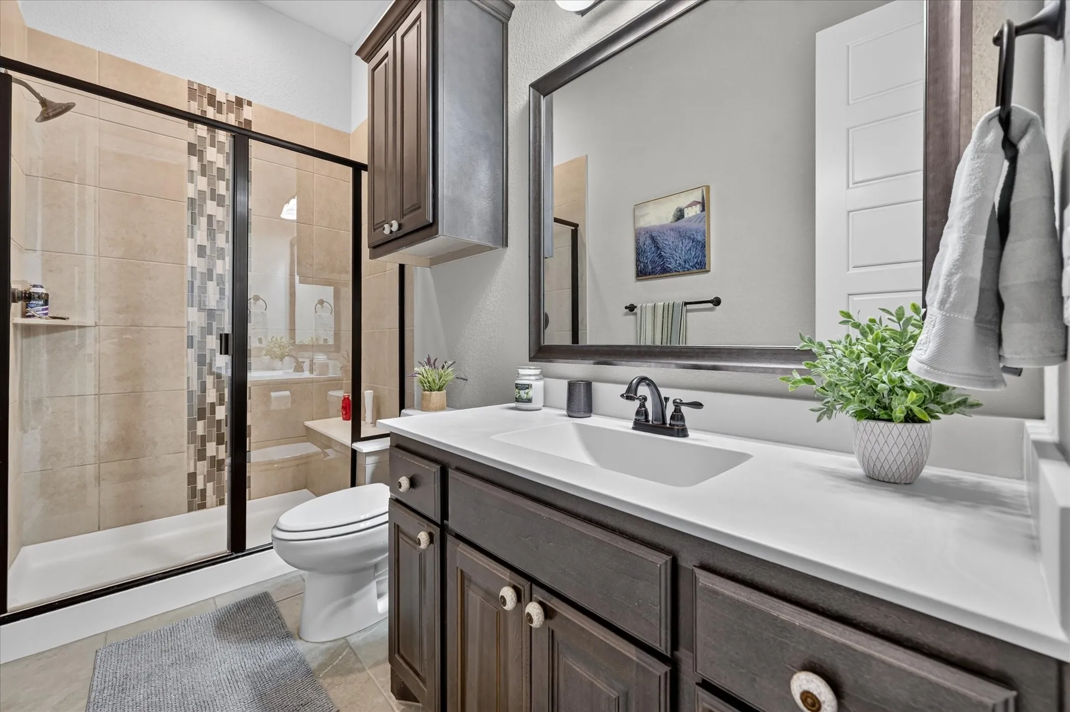 Spa-inspired bathroom featuring a dark wood vanity with white quartz countertop, dual sink configuration with matte black faucetry, and a large framed mirror