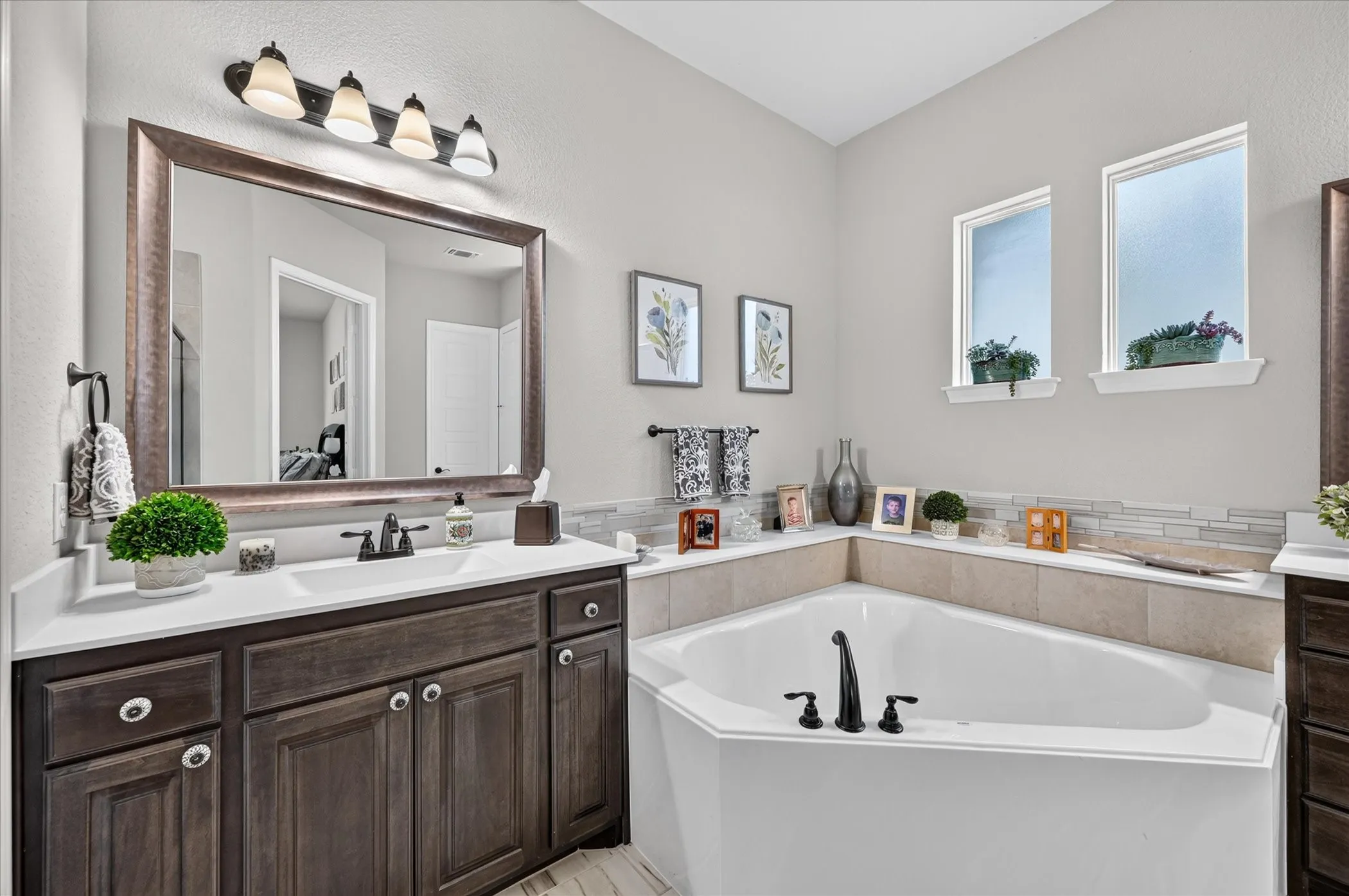 Spa-inspired primary bathroom featuring a dark wood vanity with dual sinks, framed mirror with integrated lighting, and a freestanding soaking tub with matte black fixtures