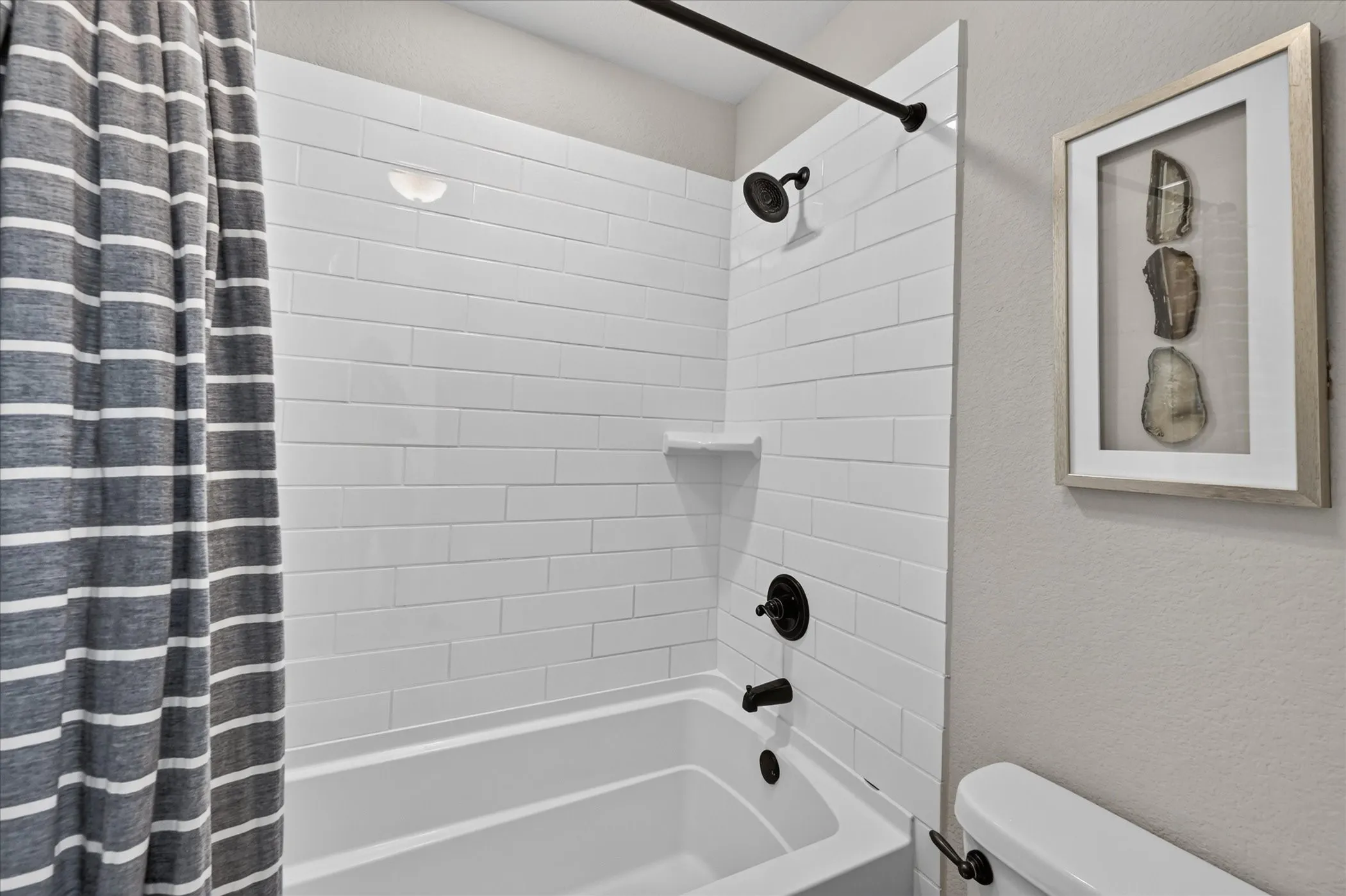 Bathtub with white subway tile surround, matte black shower fixtures, and integrated shower shelf