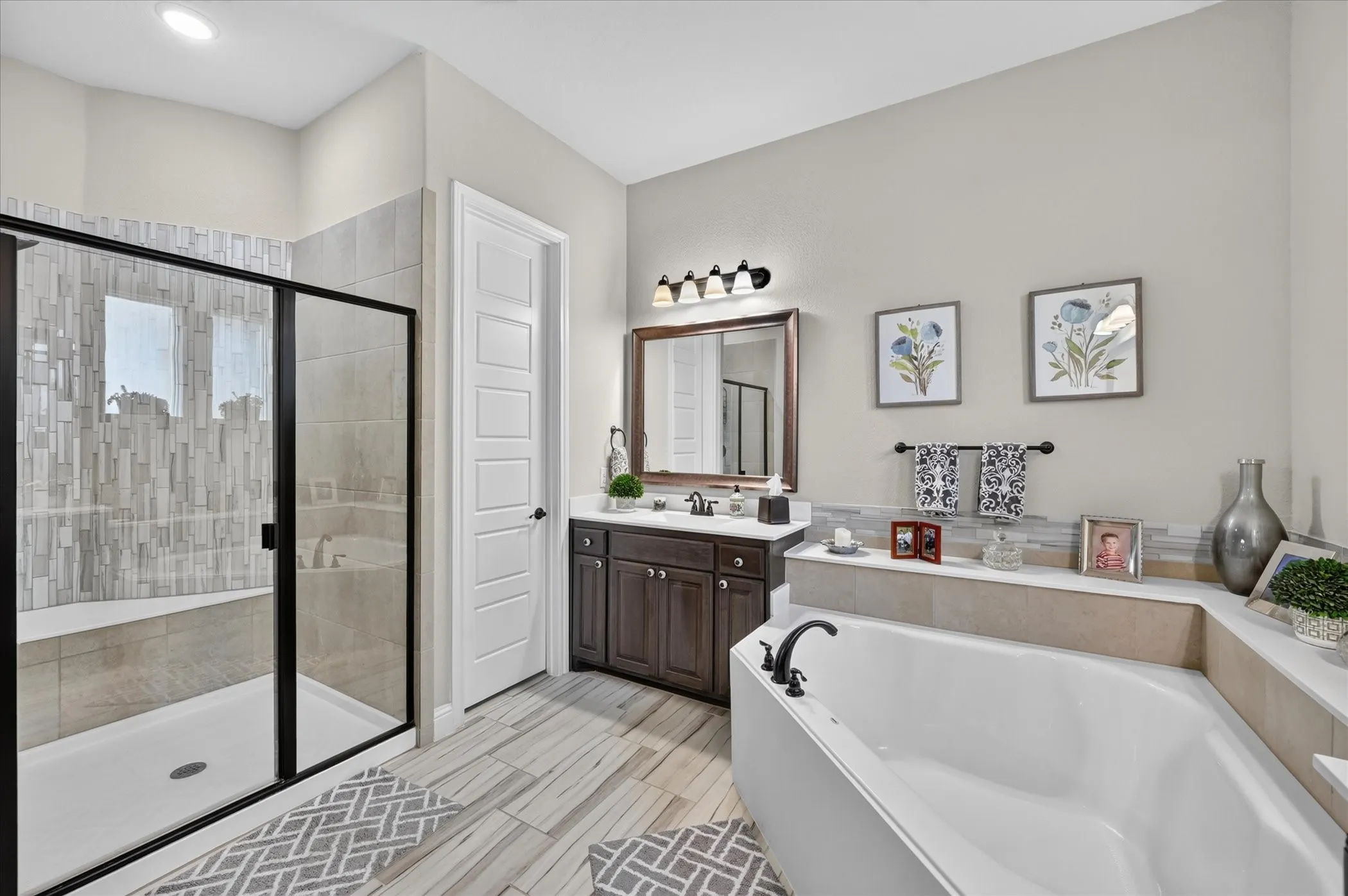 Spa-inspired primary bathroom featuring a freestanding soaking tub, walk-in shower enclosure with geometric tile surround, dark wood vanity with dual sink basins, quartz countertop, and geometric patterned tile flooring