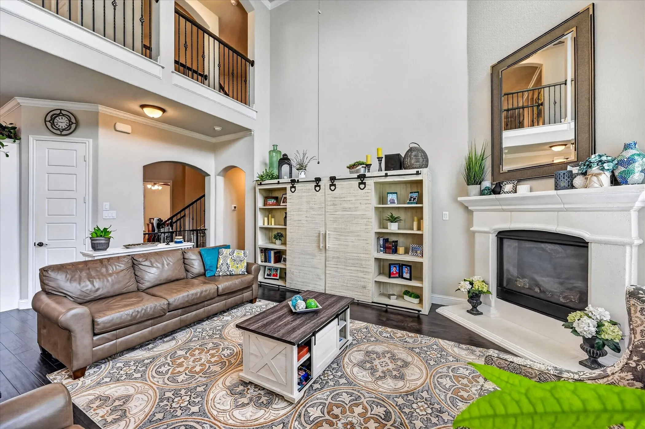 Two-story living area featuring a fireplace with hearth, dark wood-finish flooring, and an upper-level balcony with metal railings