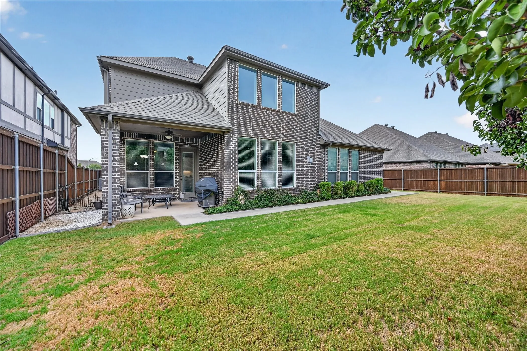 Expansive backyard featuring a covered patio, brick exterior, multiple large windows, and a wood privacy fence