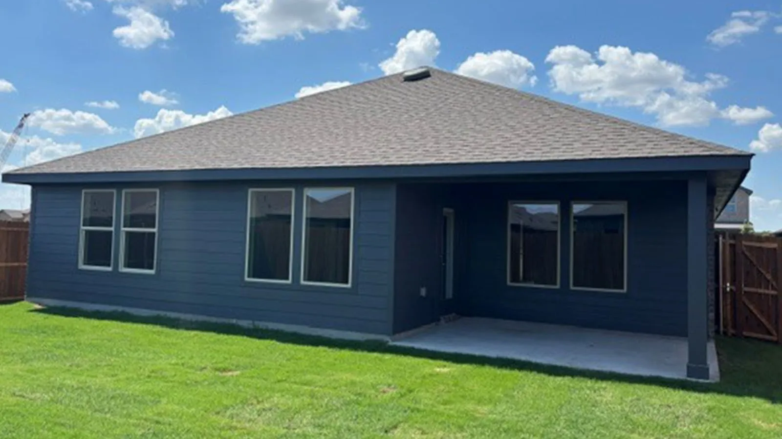 Expansive backyard featuring a manicured lawn, dark blue siding, covered patio, and a privacy fence