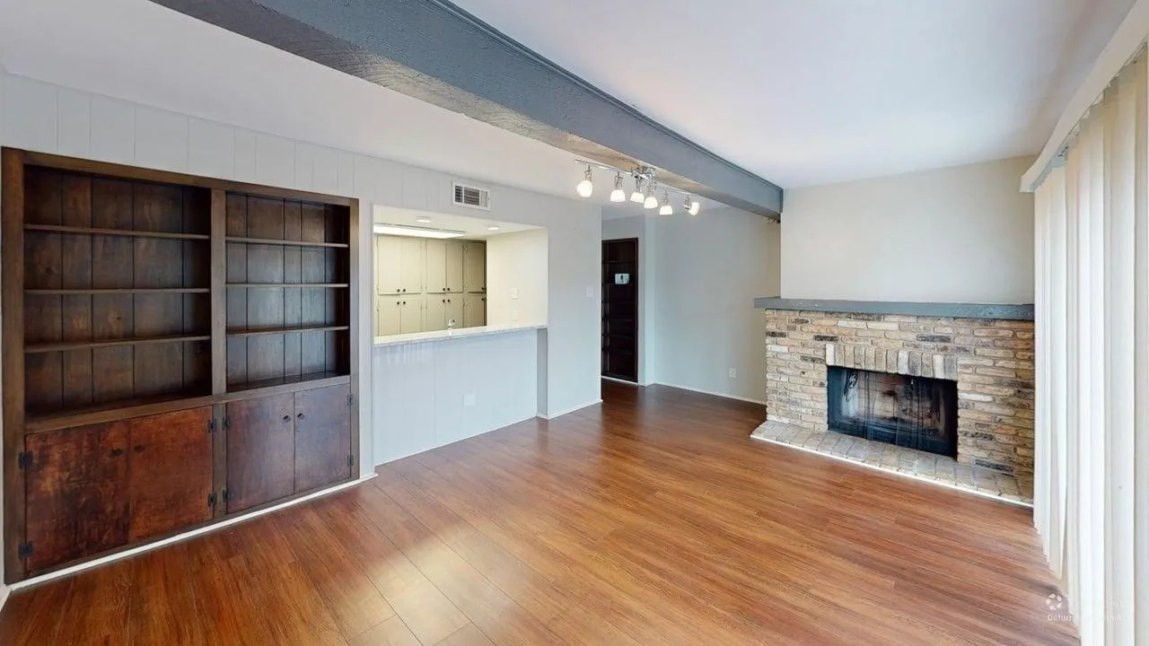 Hardwood-finish flooring, built-in shelving with cabinetry, a brick fireplace with a stone hearth, and track lighting