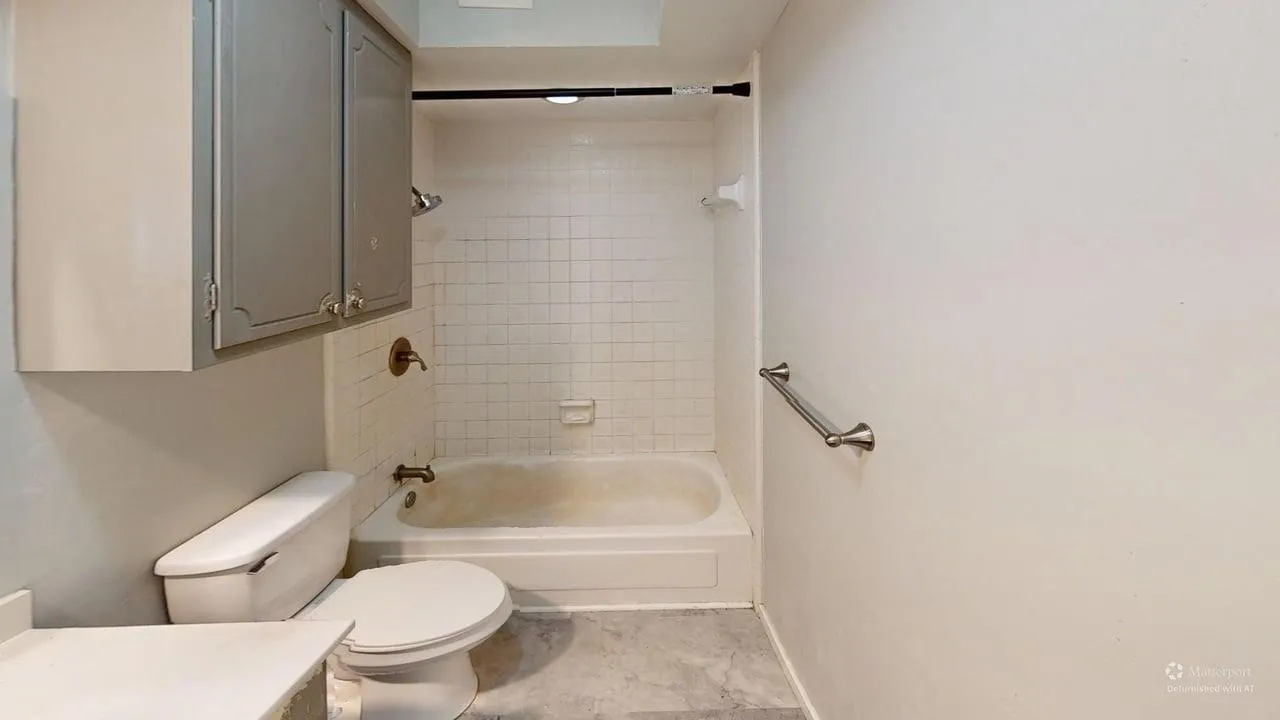 Bathtub with ceramic tile surround, toilet, and overhead cabinetry