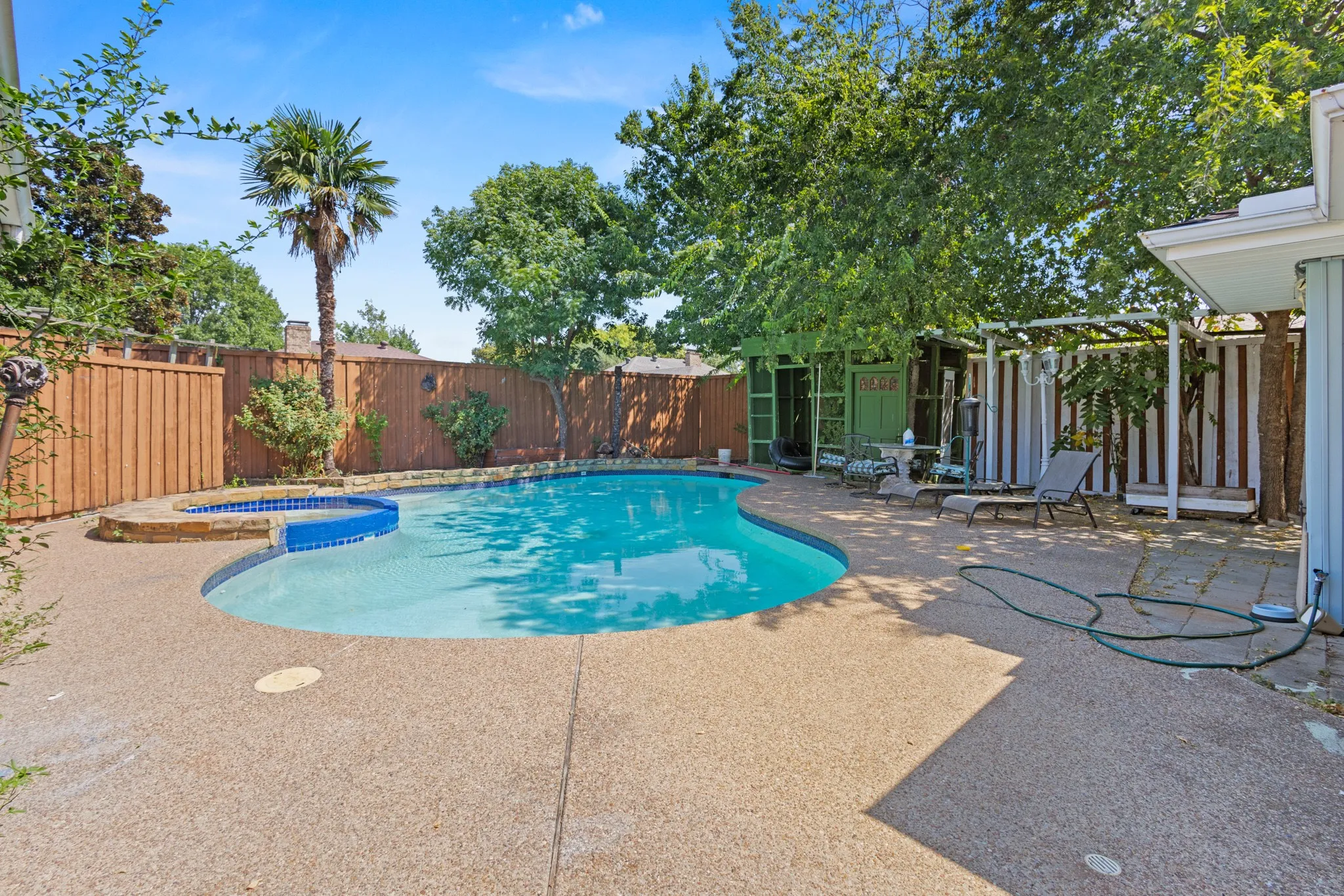 Sparkling resort-style pool with sun shelf and integrated spa featuring crystal-blue water, surrounded by expansive concrete decking