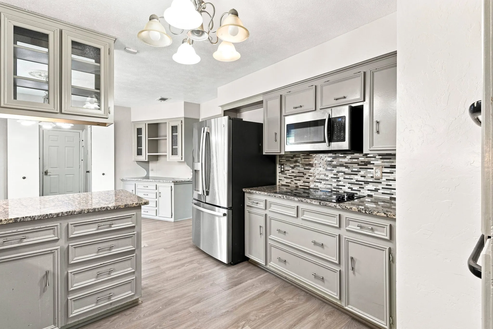 Kitchen featuring light-toned cabinetry, granite-finish countertops, stainless steel appliances, a patterned tile backsplash, and wood-finish flooring