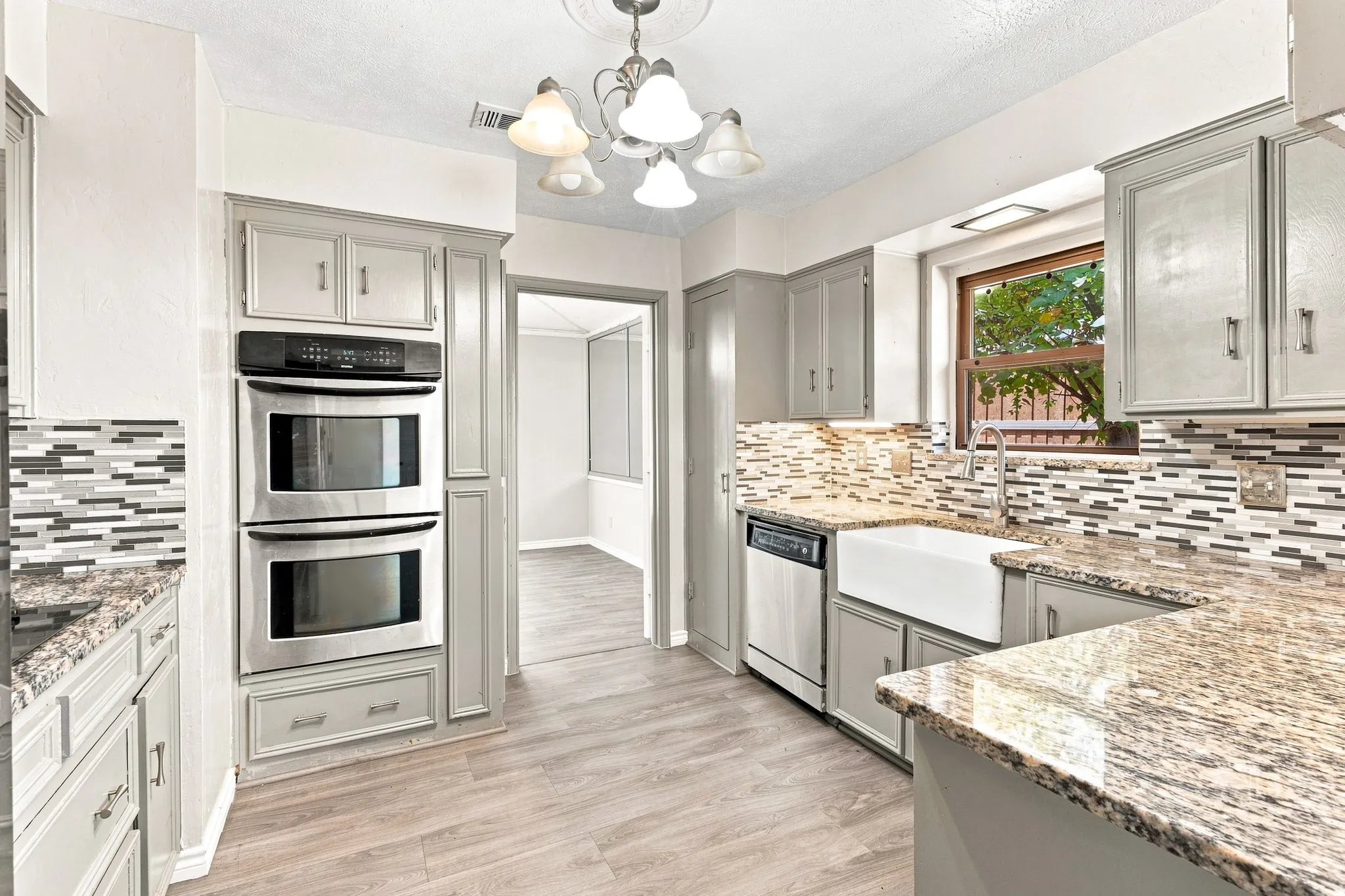 Kitchen featuring gray cabinetry, stainless steel double wall ovens, a farmhouse sink, granite countertops, and wood-finish flooring