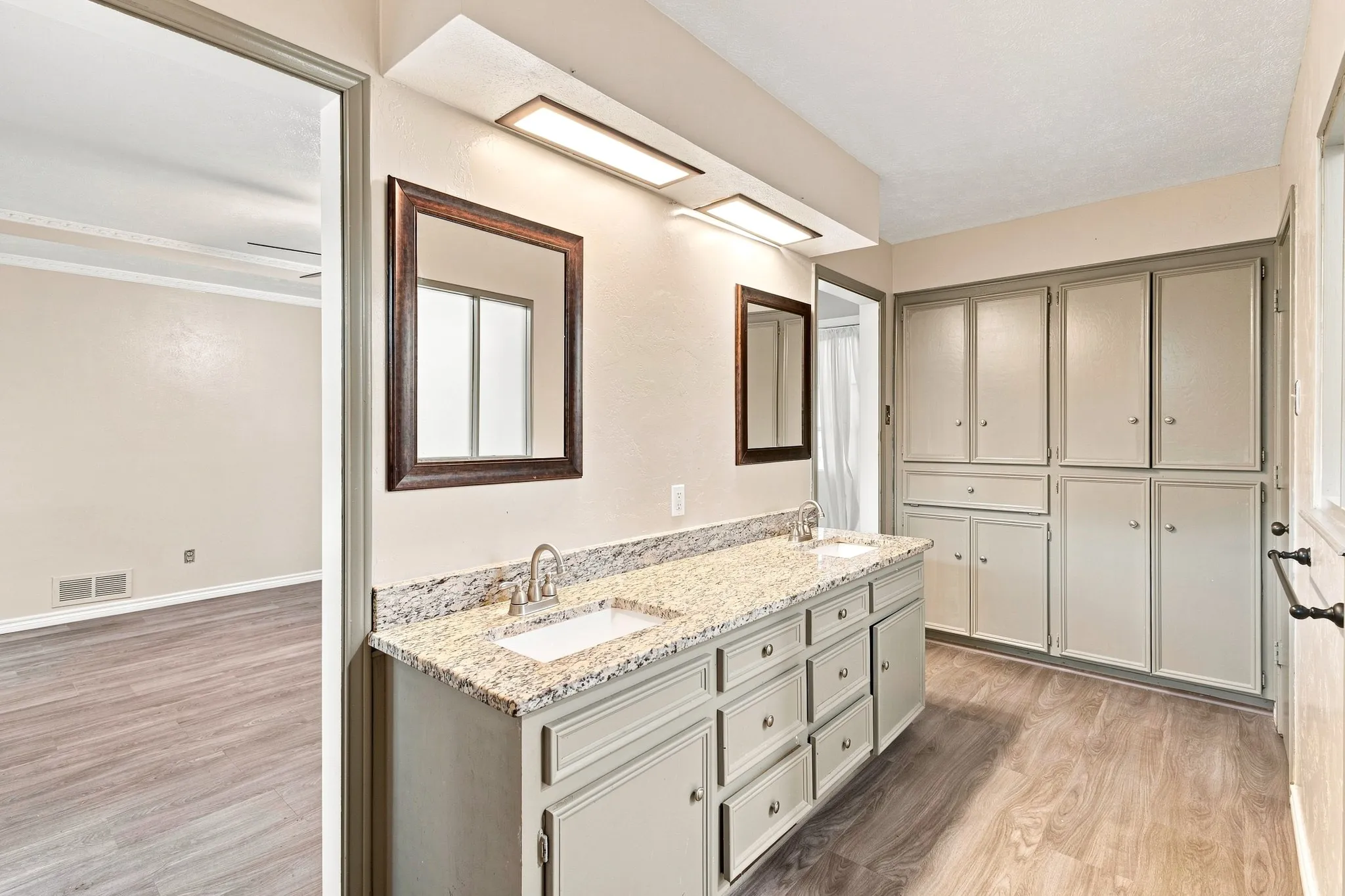 Spa-inspired primary bathroom featuring a long vanity with multiple drawers and a granite countertop, dual framed mirrors with integrated lighting, and wood-finish flooring