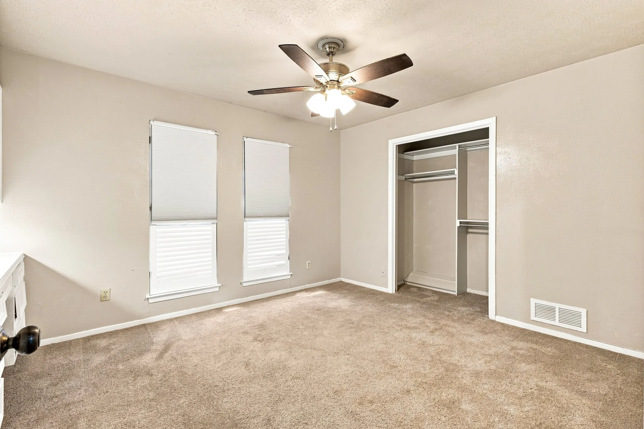 Carpeted room with neutral wall paint, two windows with blinds, a ceiling fan, and an open closet with shelving and hanging rods