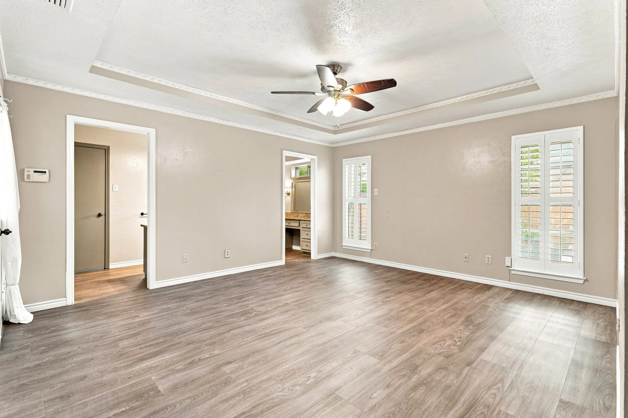 Wood-finish flooring, tray ceiling with a ceiling fan, and two windows with plantation shutters