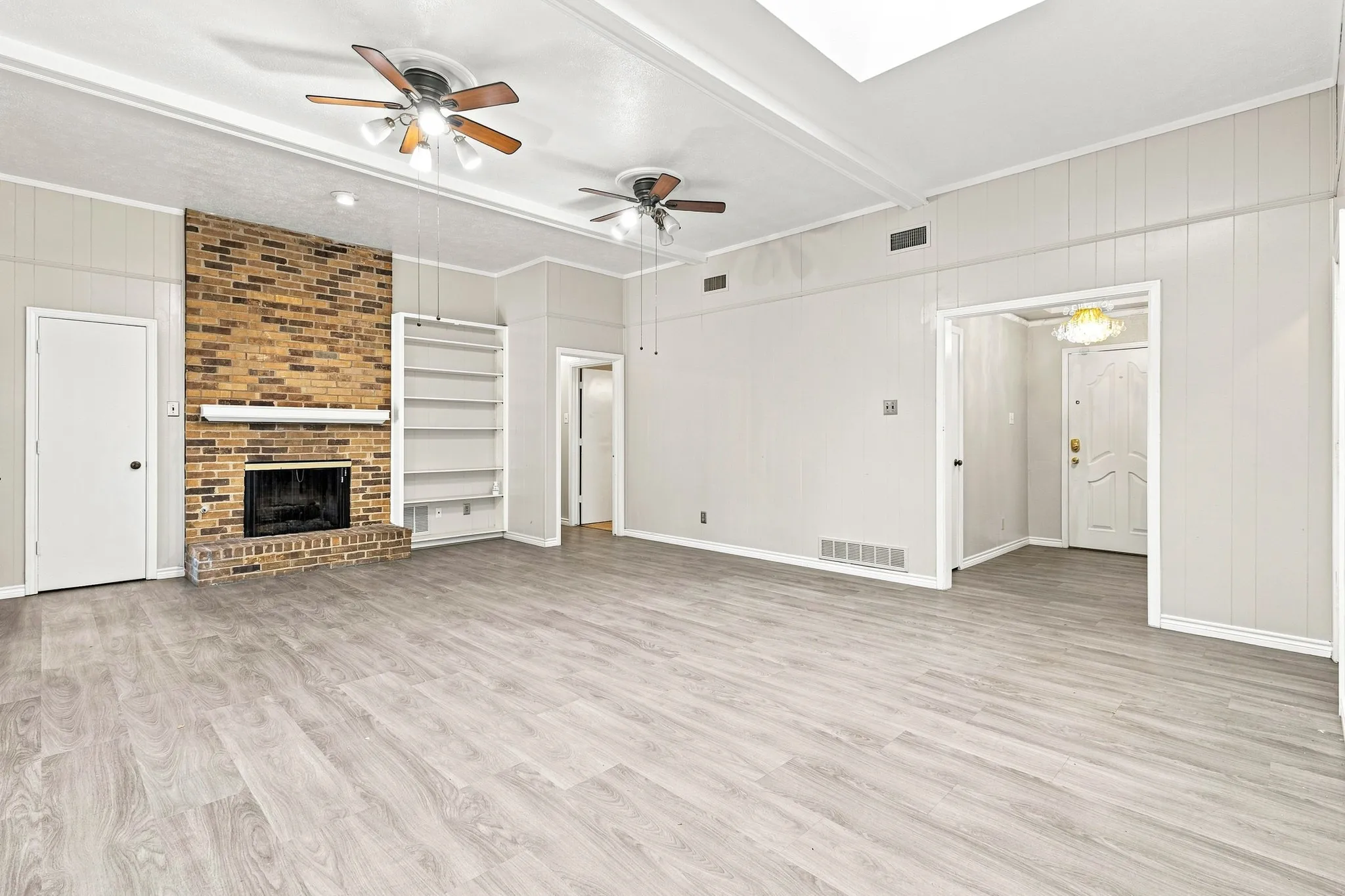 Light wood-finish flooring, brick-surround fireplace, built-in shelving, white paneling, and ceiling fans