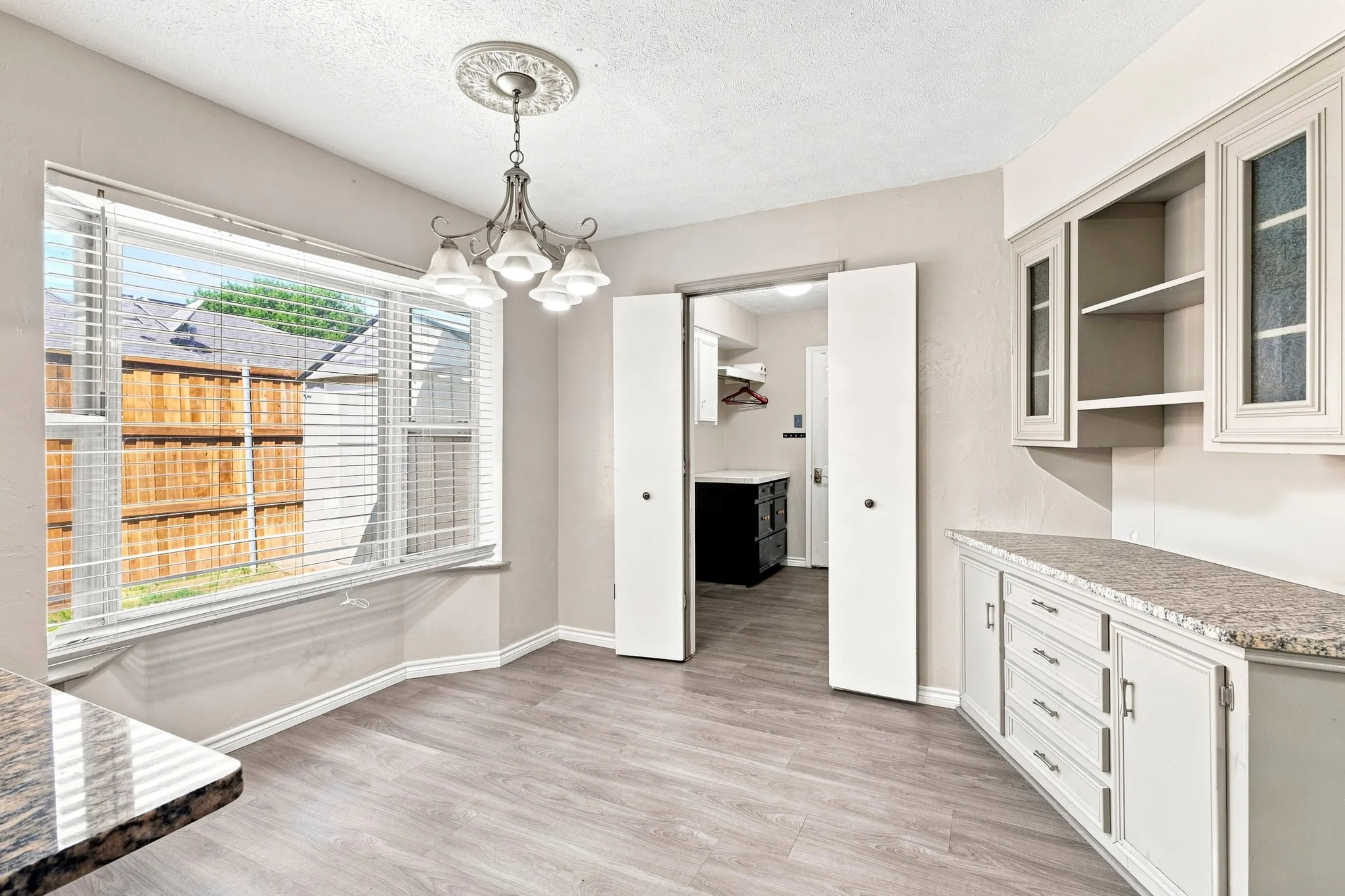 Bay window with blinds, wood-finish flooring, built-in cabinetry with stone countertops, decorative ceiling medallion, and a four-light chandelier