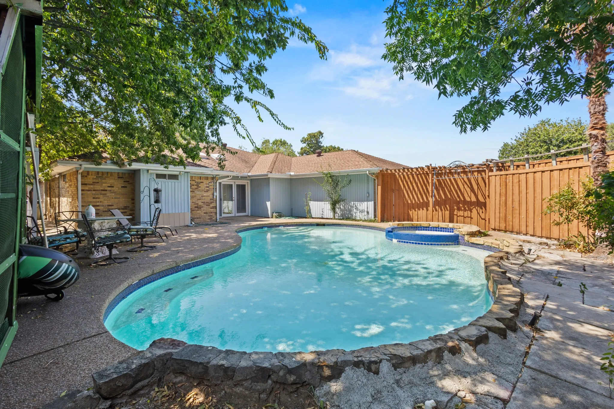 Backyard oasis featuring a freeform swimming pool, integrated spa, surrounding concrete patio, and a privacy fence