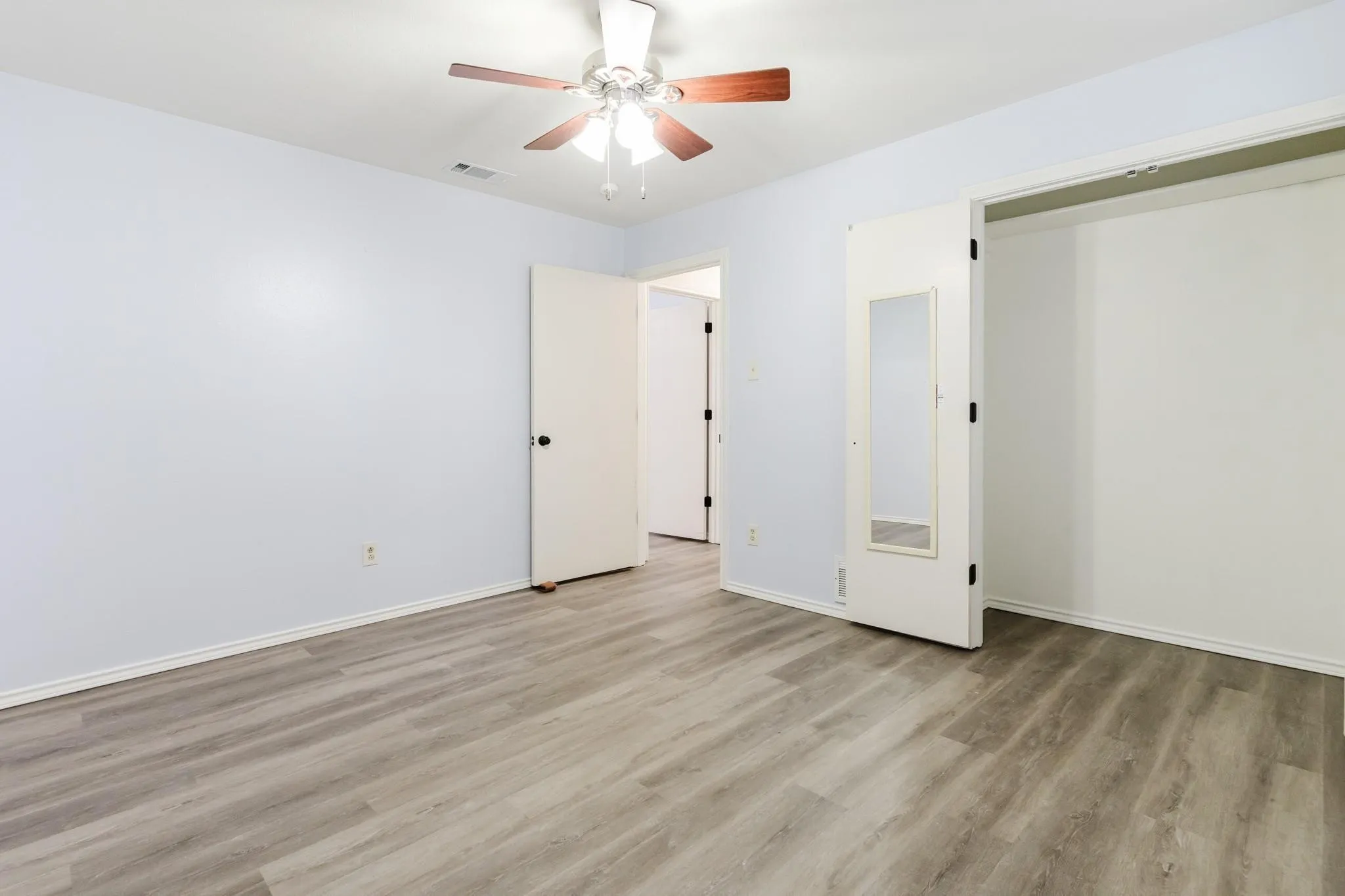 Wood-finish flooring with light-toned walls, ceiling fan, and built-in closet with mirrored door