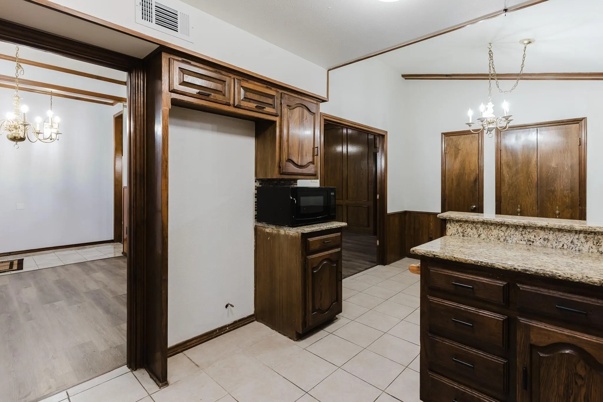 Kitchen featuring wood-finish cabinetry, light-toned granite countertops, and light-toned tile flooring