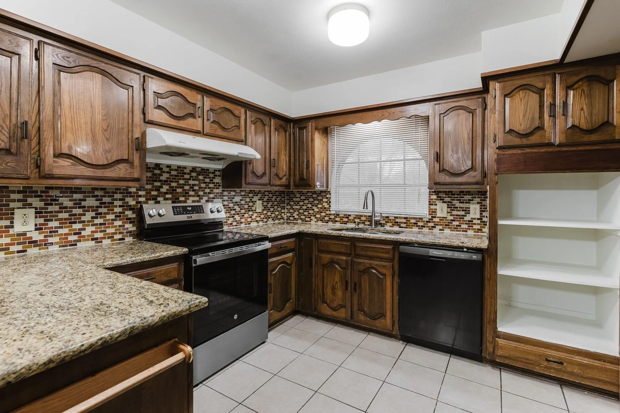 Kitchen featuring granite-style countertops, wood cabinetry, tile flooring, and a tile backsplash