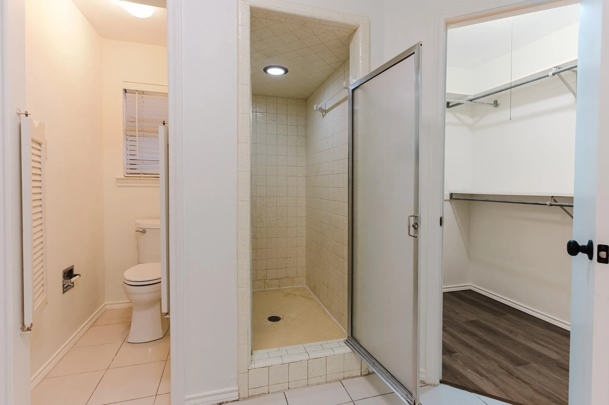 Tiled shower enclosure with a glass door, recessed lighting, and a separate water closet with a window