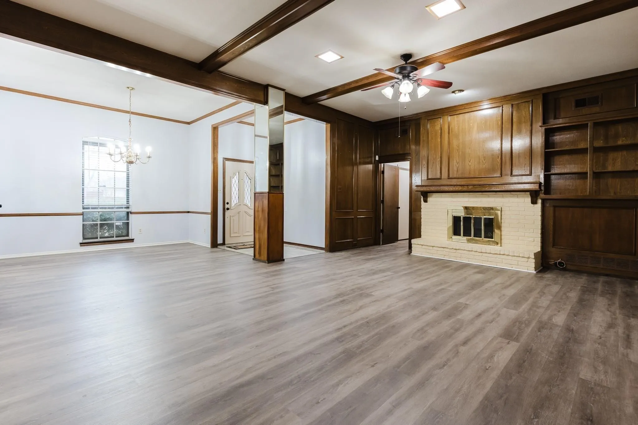 Wood-finish flooring throughout, wood-paneled walls, built-in shelving, brick fireplace, and a ceiling fan