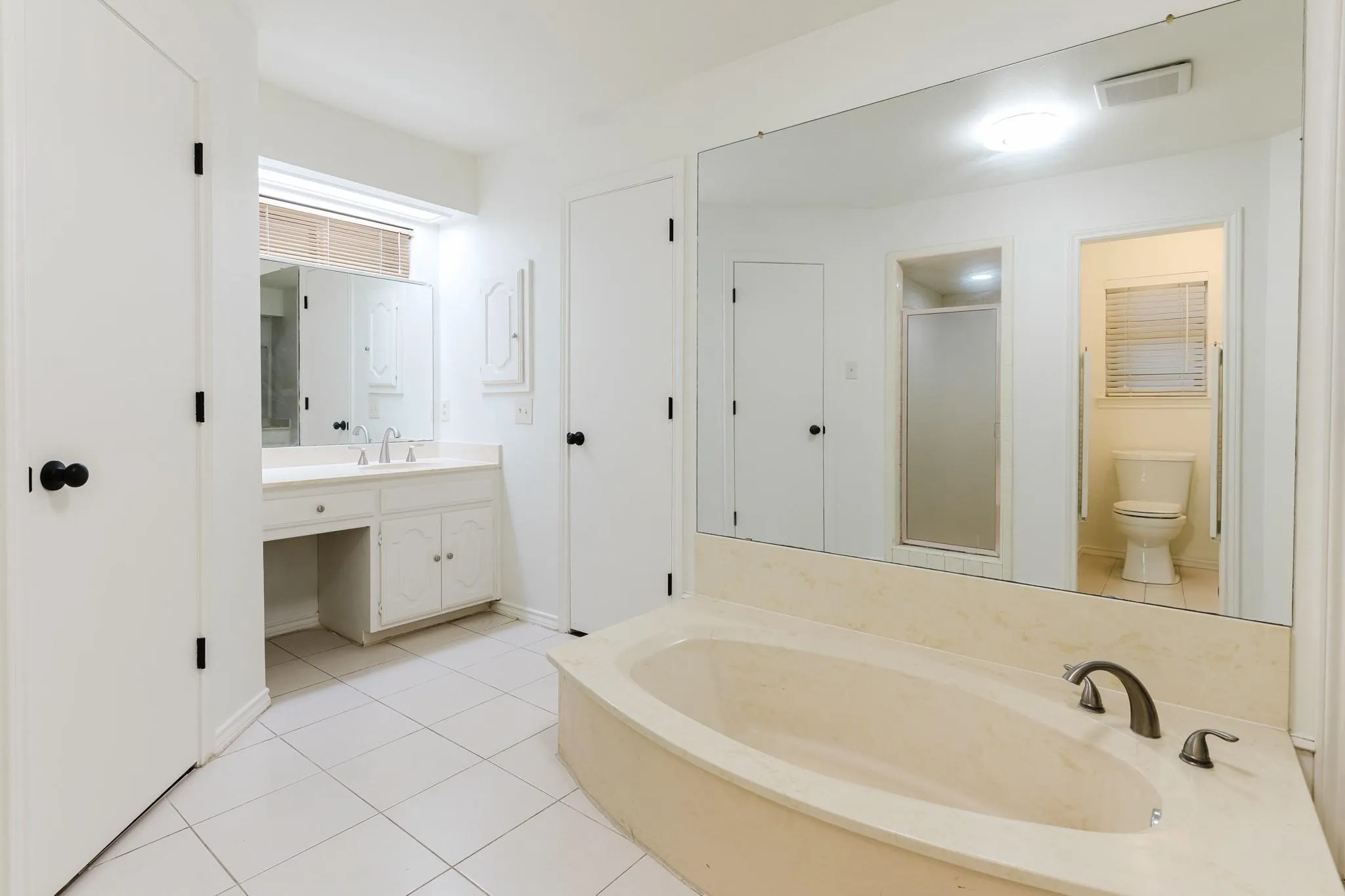 White tile flooring throughout, with a built-in soaking tub, a vanity with dual sinks, and a separate shower enclosure