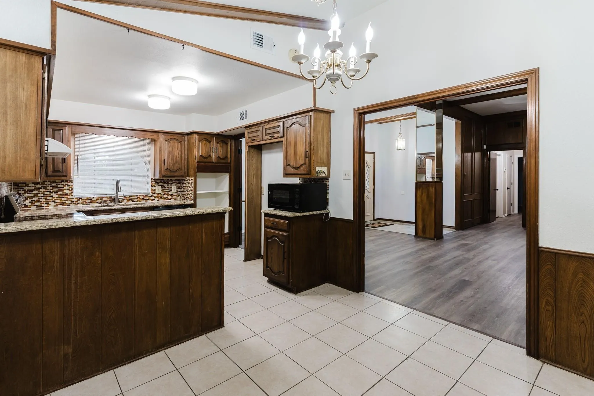 Kitchen featuring wood-finish cabinetry, a peninsula with a granite-style countertop, mosaic tile backsplash, and ceramic tile flooring