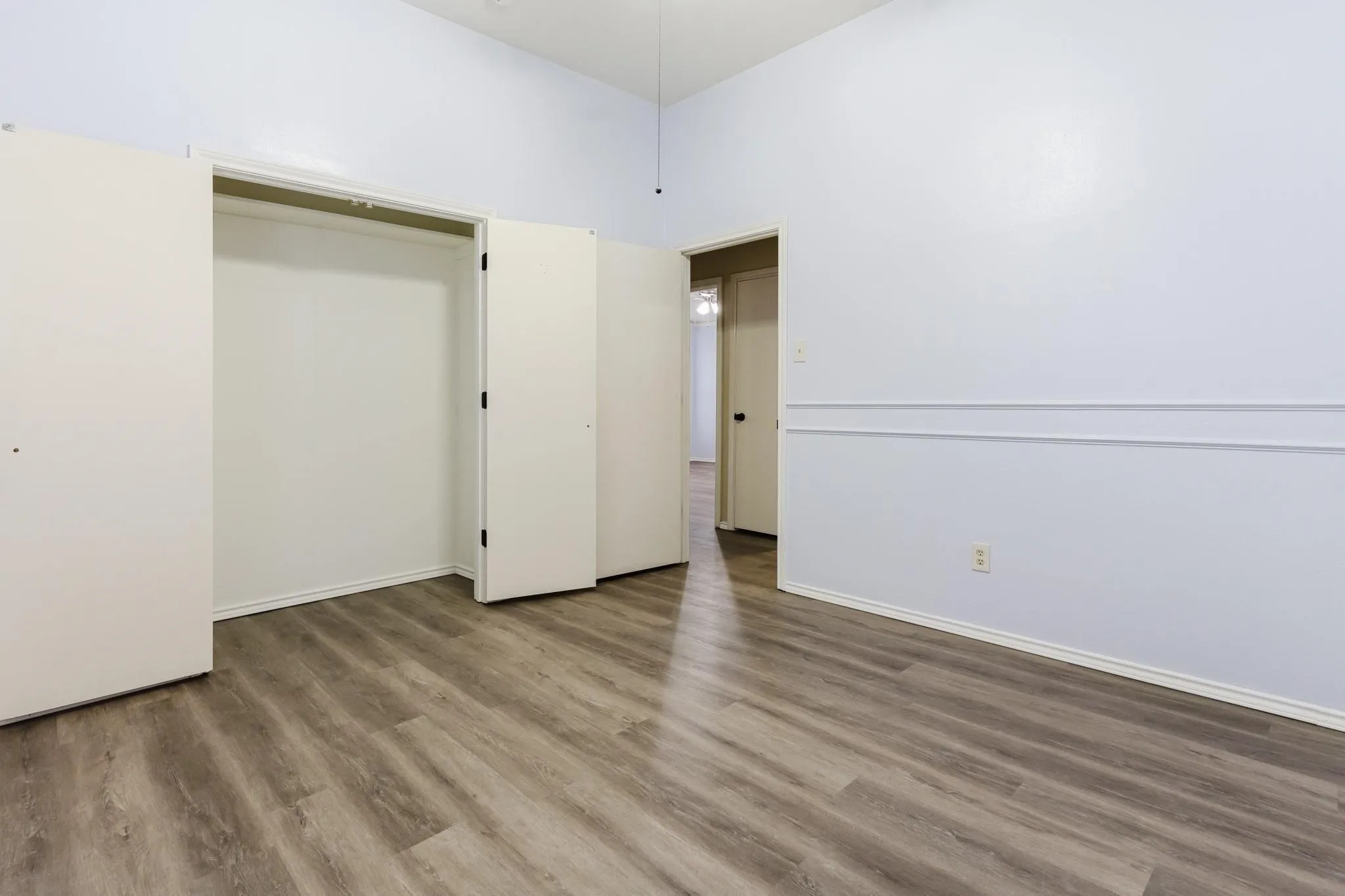 Wood-finish flooring, accent wall molding, a vaulted ceiling, and an open closet with bi-fold doors