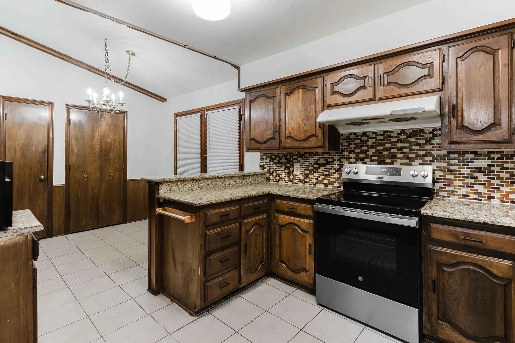 Kitchen featuring wood-finish cabinetry, granite countertops, a built-in range, a tile backsplash, and tile flooring
