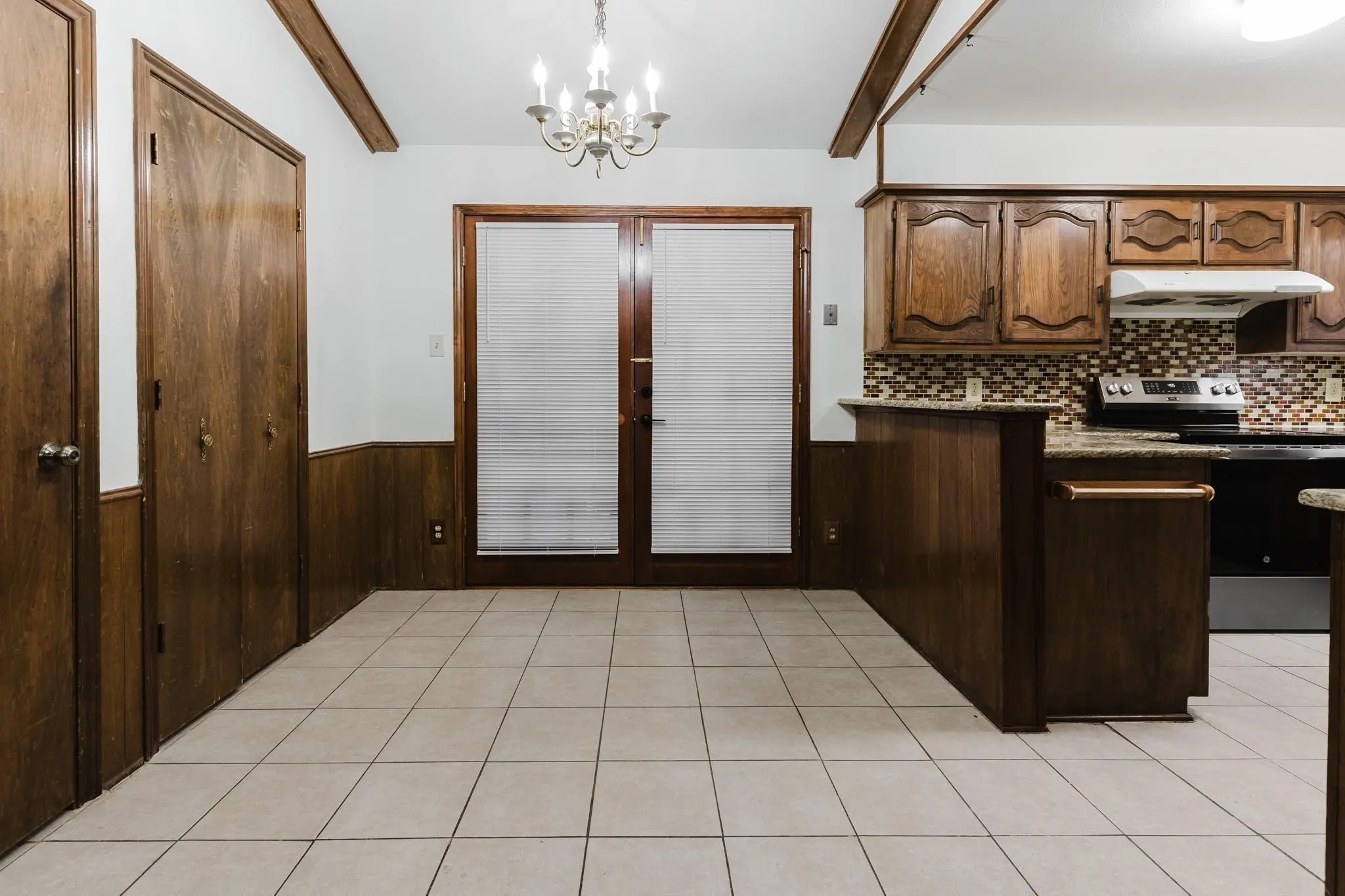 Tile flooring, exposed wood ceiling beams, wood-paneled walls, wood double doors, and a chandelier