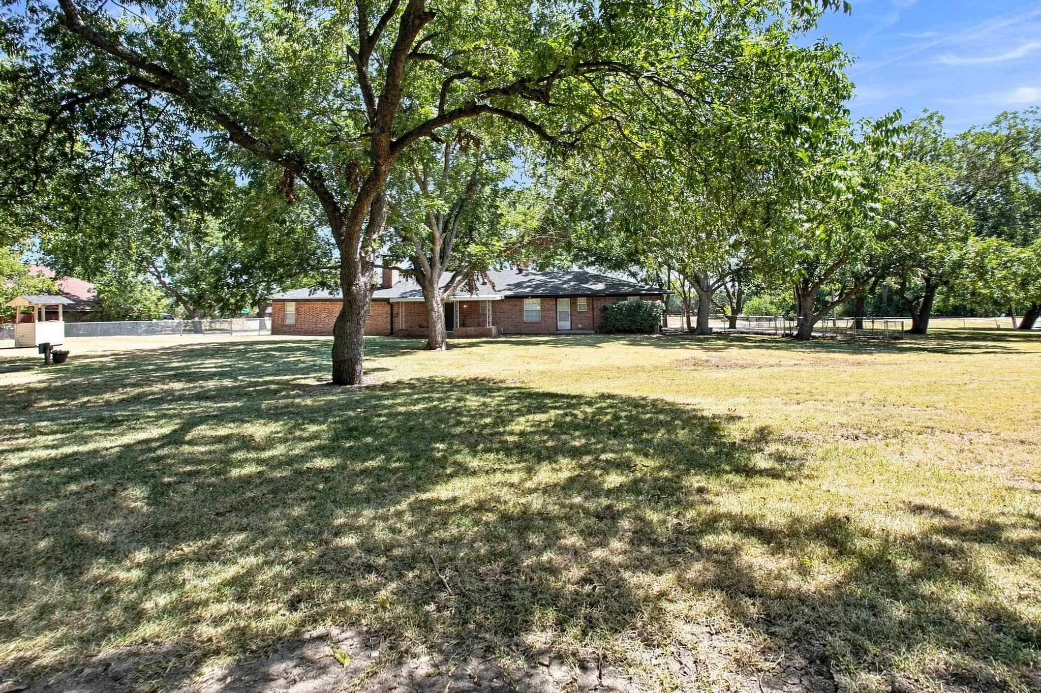 Sprawling property with the home nestled beneath mature pecan shade trees and a water well seen in the left of the photo
