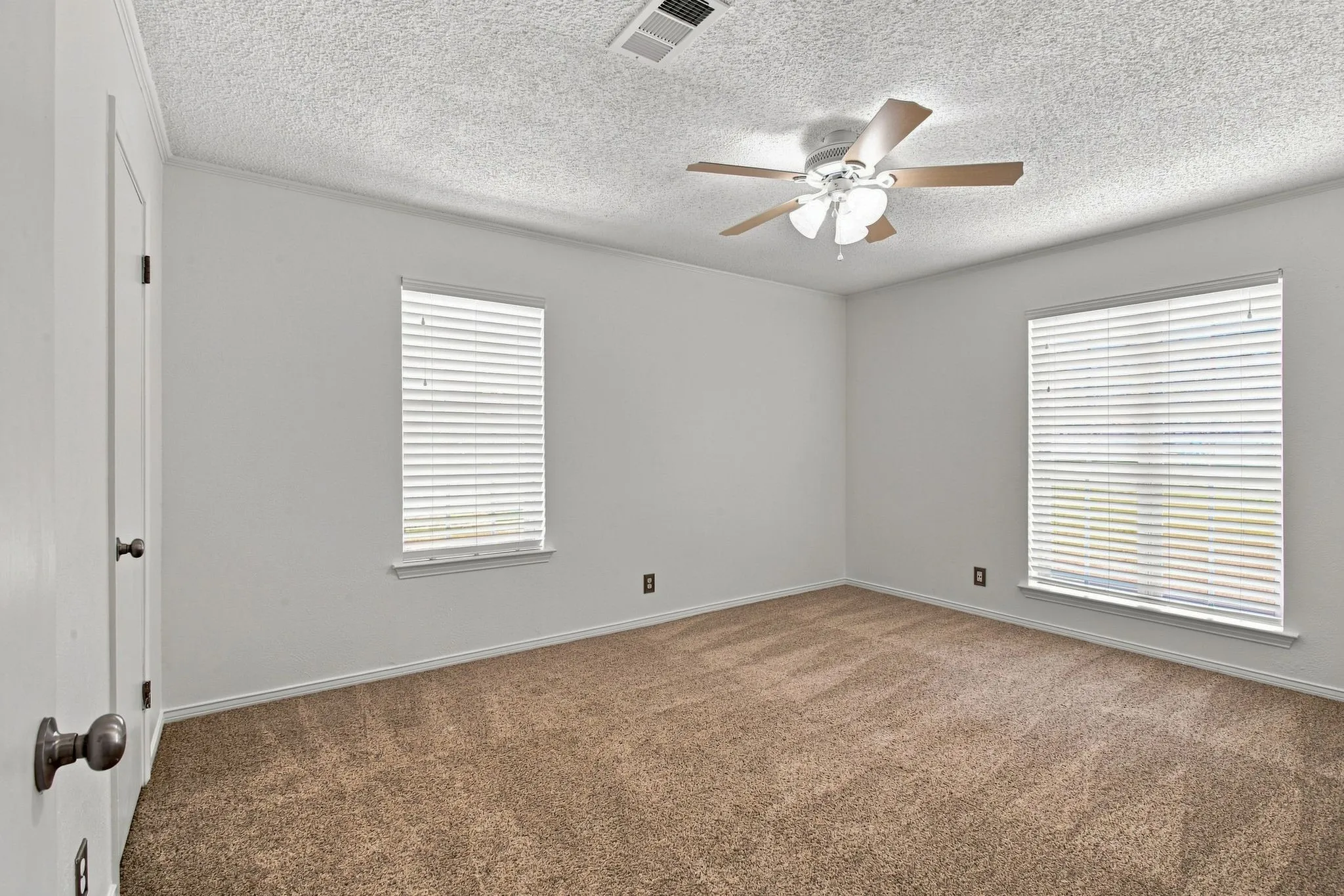 Bedroom with ceiling fan, two windows with blinds, and carpeted flooring