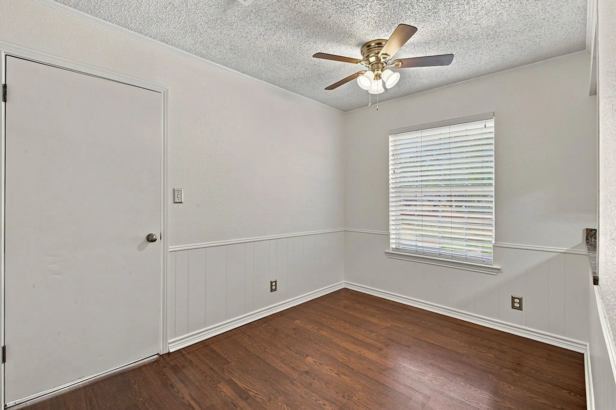 Wood-finish flooring, wainscoting details, ceiling fan with integrated lighting, and window blinds