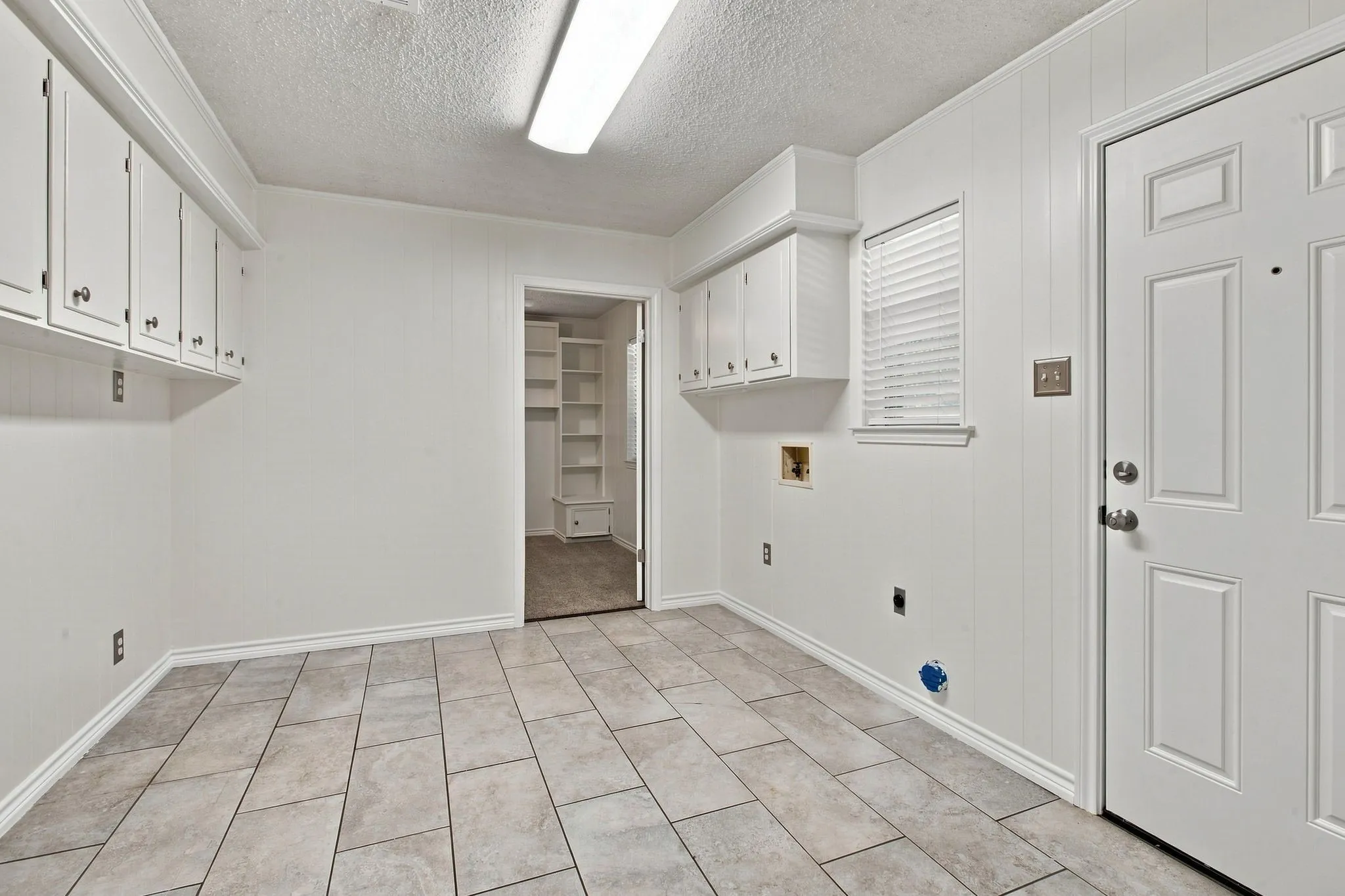 Tile flooring, white cabinetry, paneled walls, ceiling-mounted fluorescent lighting, and a door to the garage and door to the backyard