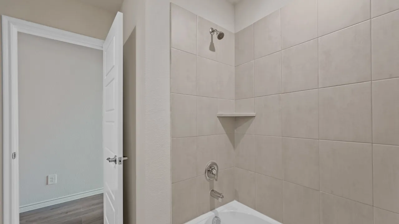 Shower/tub combination with light-toned rectangular tile surround, built-in corner shelf, and chrome fixtures