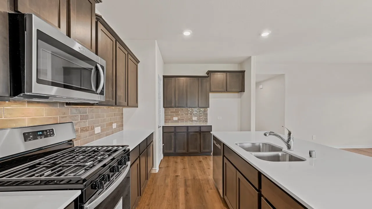 Kitchen featuring wood-finish flooring, stainless steel appliances, dark wood cabinetry, white countertops, and a double basin sink