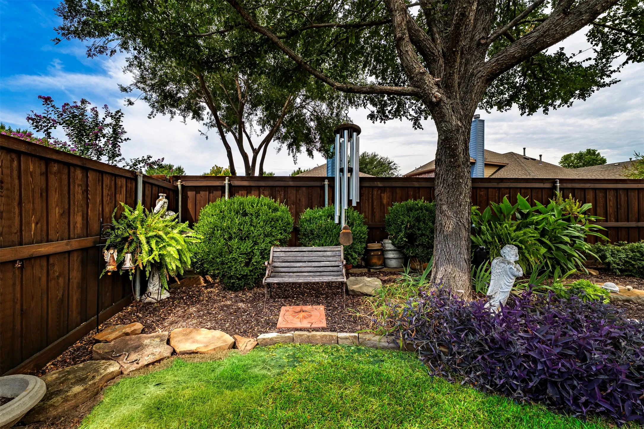 Mature landscaped backyard featuring a lush lawn, wood privacy fencing, specimen shade trees, and mixed plantings including ornamental shrubs and flowering perennials