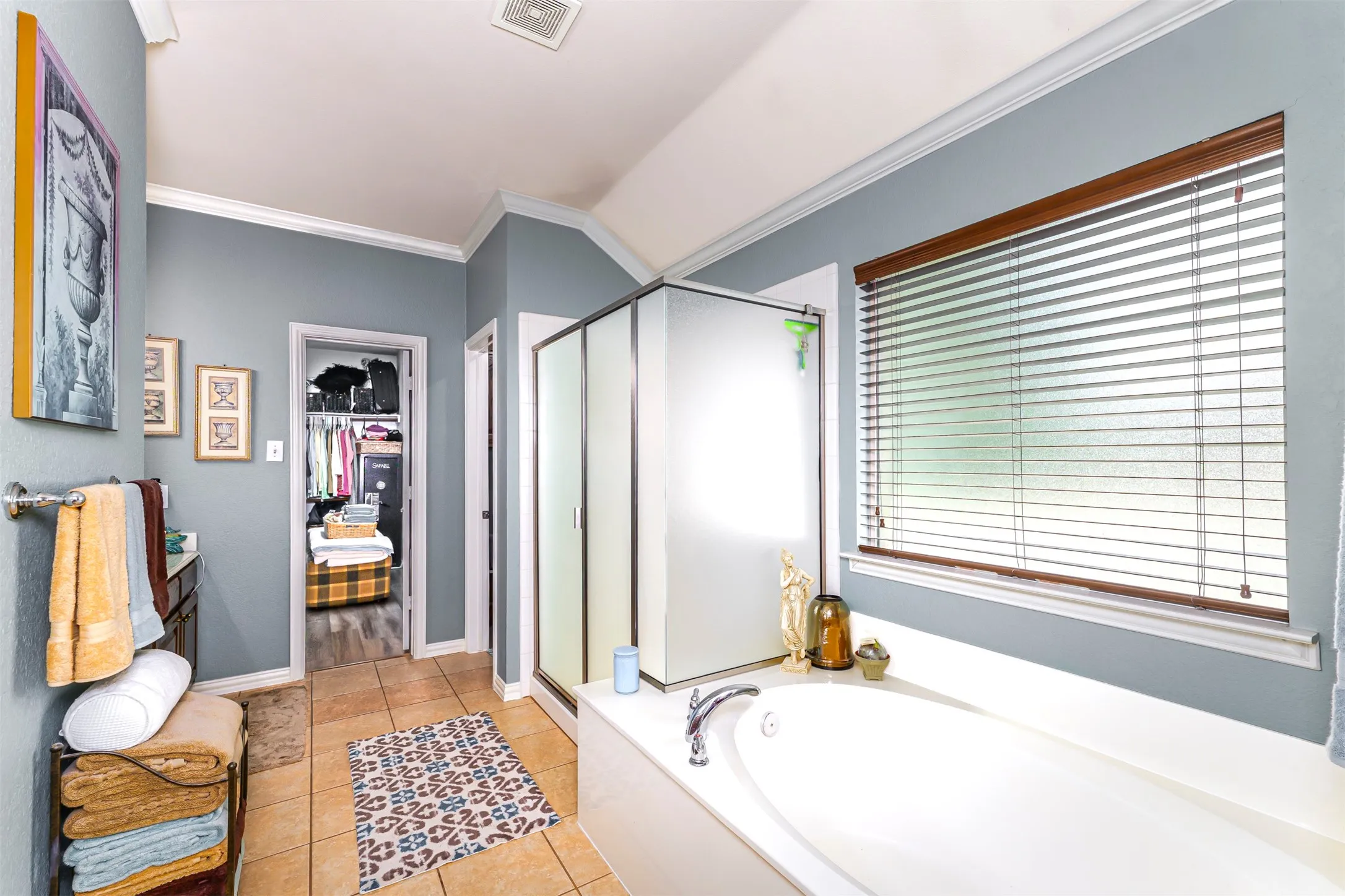 Built-in soaking tub, separate glass-enclosed shower, light-colored tile flooring, and a large window with blinds