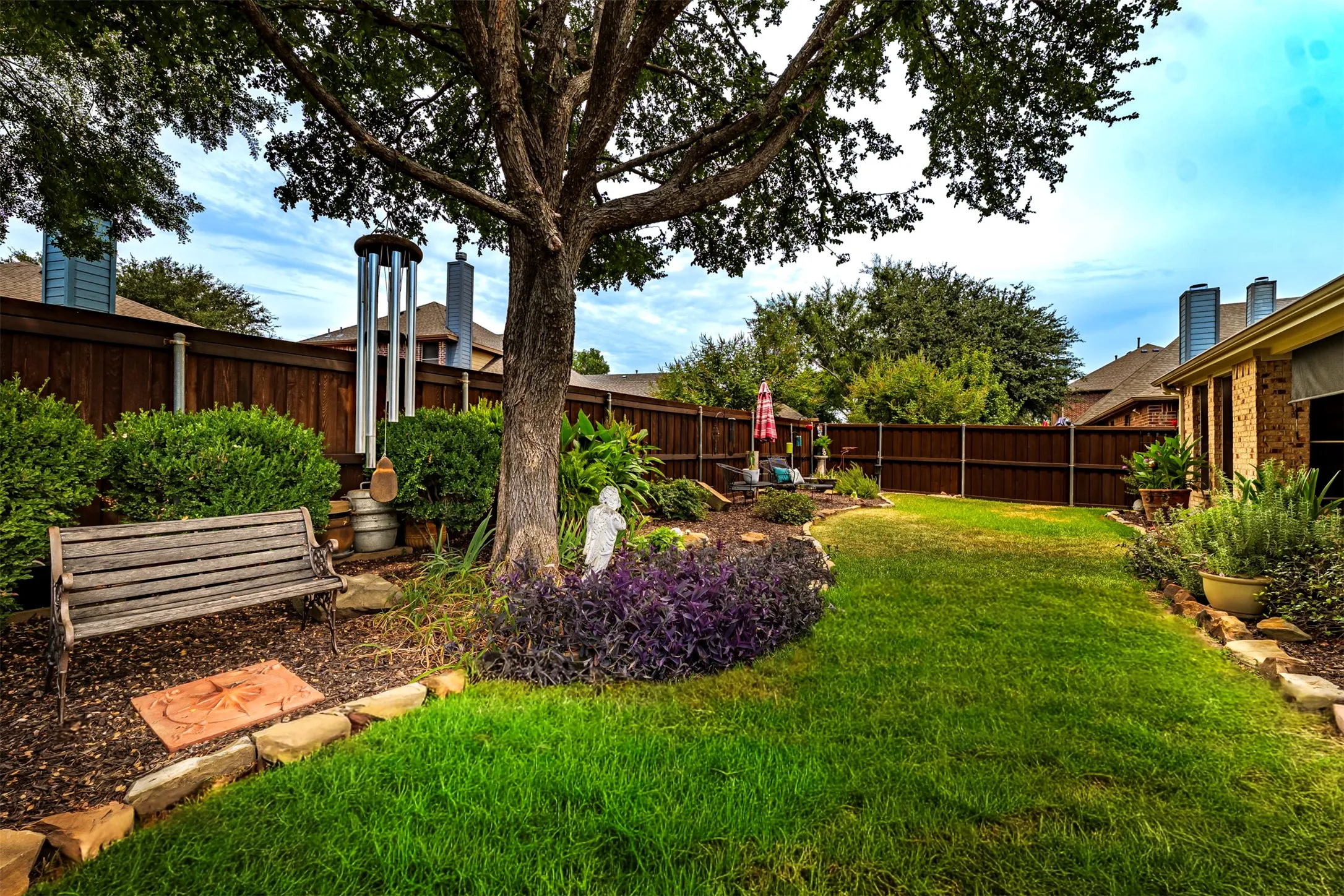 Expansive backyard featuring a manicured lawn, established tree, and a wood privacy fence