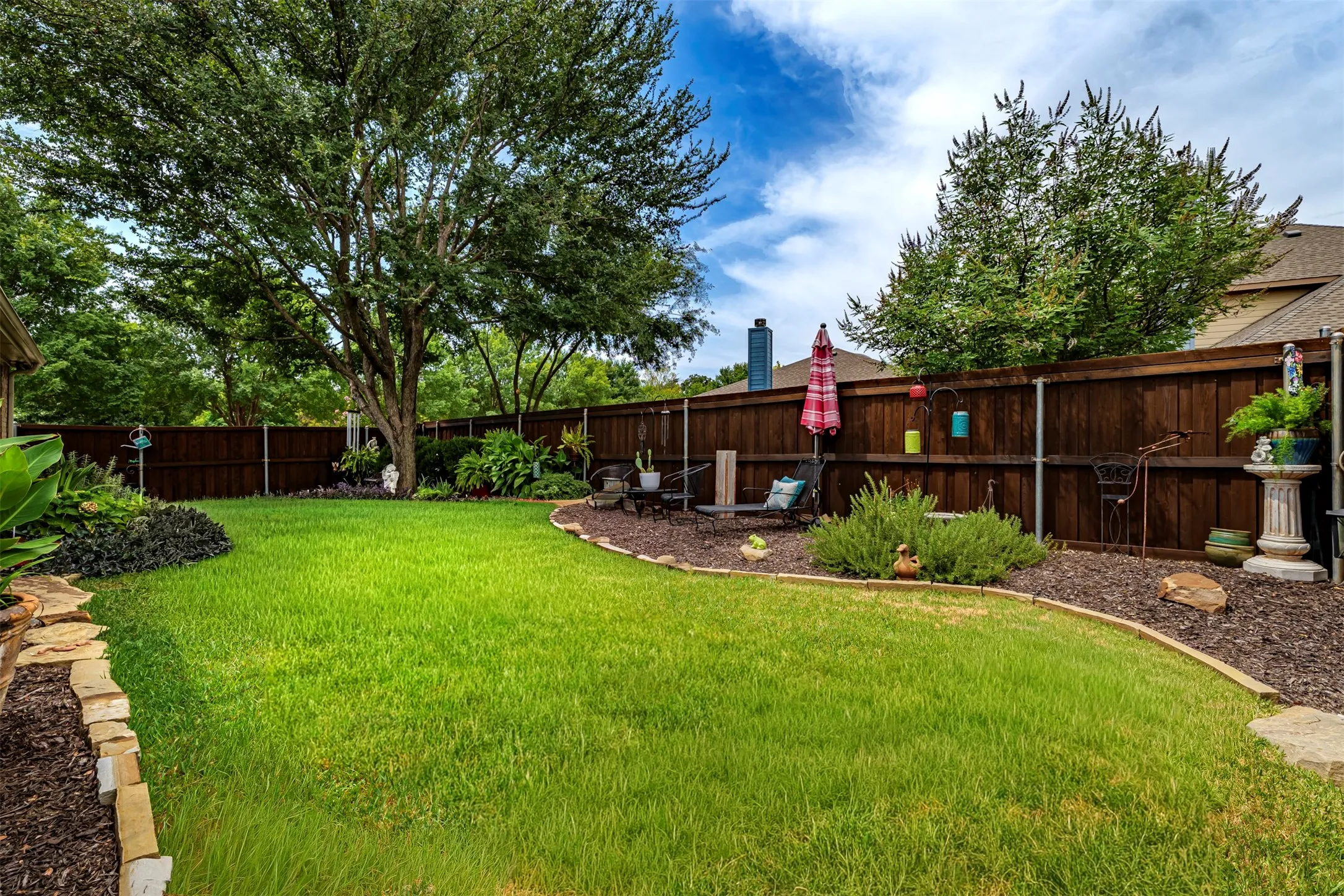 Expansive green lawn with a mature tree, stone-edged flower beds, and a wood privacy fence