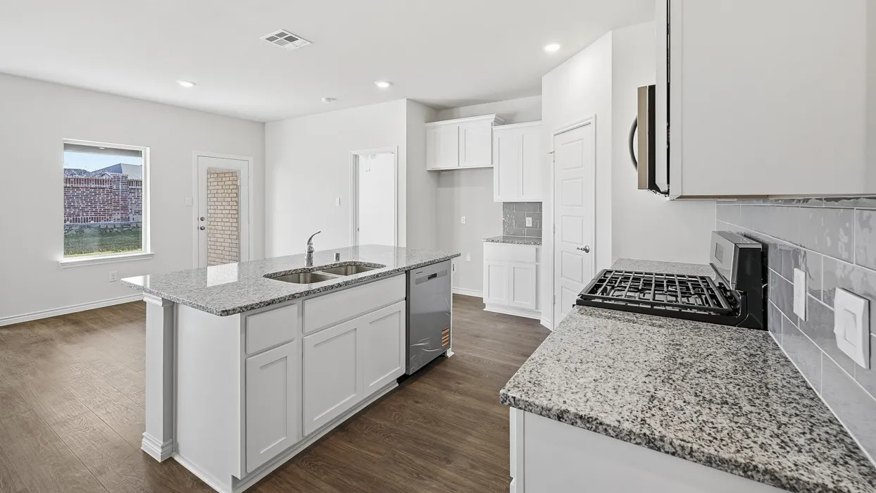 Kitchen with wood-finish flooring, white cabinetry, a central island featuring a double-basin sink, and granite countertops