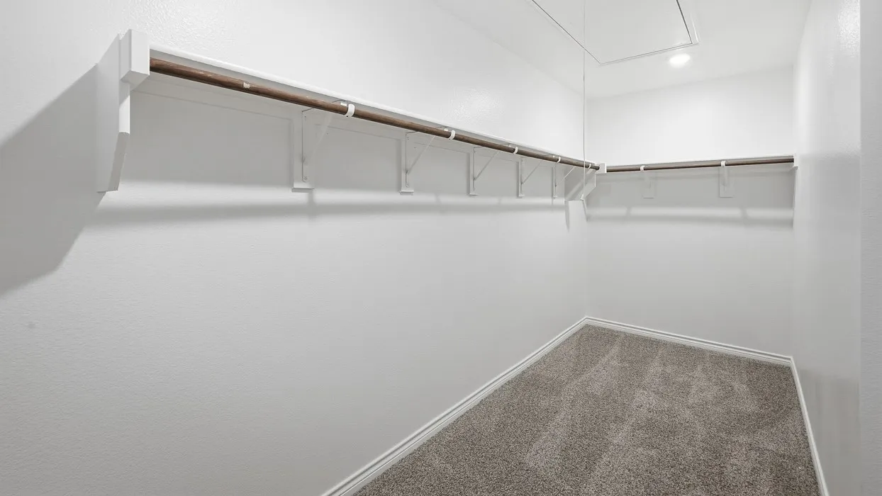 Well-lit interior closet featuring wall-mounted hanging rods, white shelving, and grey carpet flooring