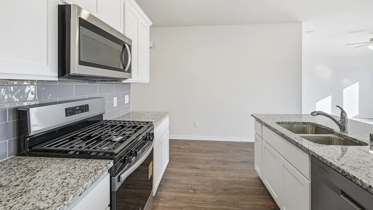 Kitchen featuring white cabinetry, granite countertops, a stainless steel microwave, and a gas range
